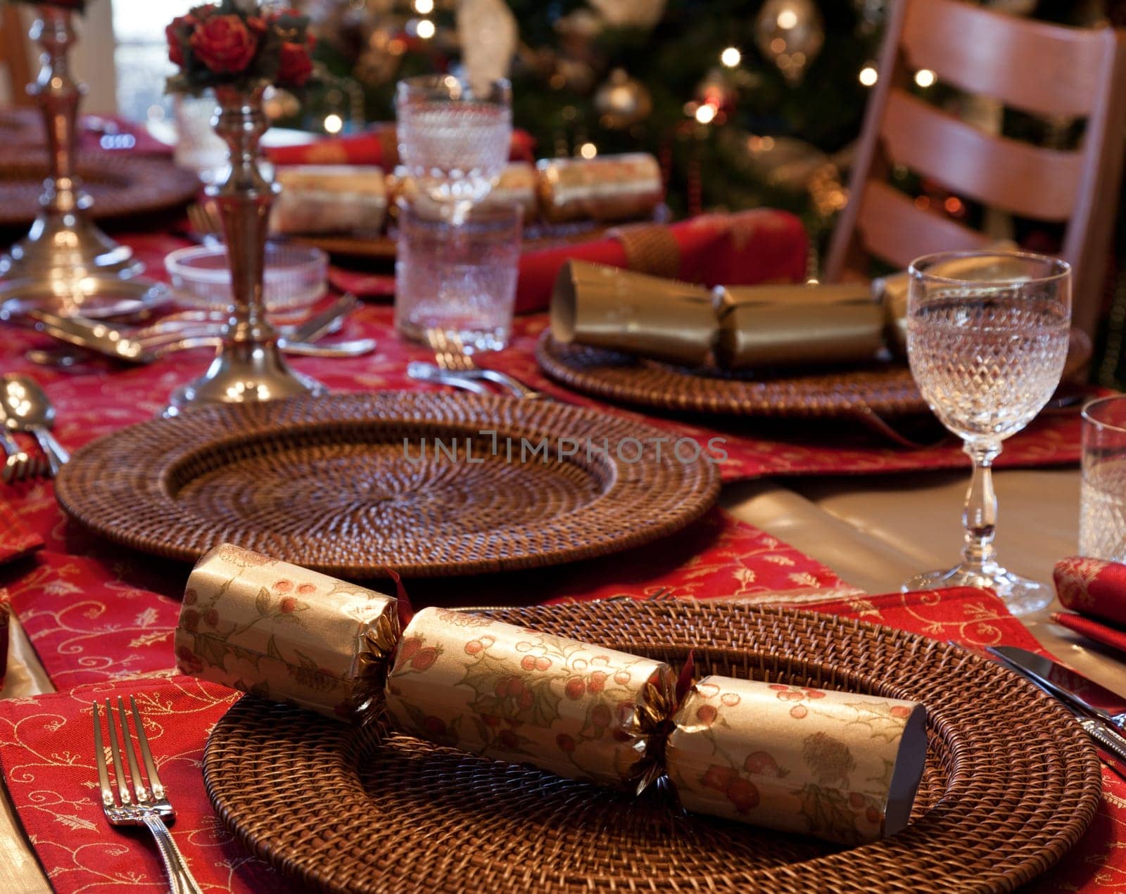Christmas crackers on table set for Christmas lunch with candles and tree in background