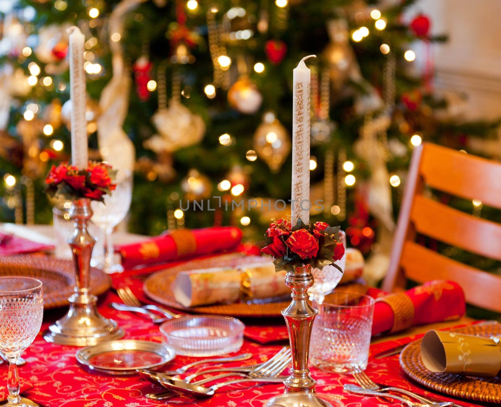 Christmas crackers on table set for Christmas lunch with candles and tree in background