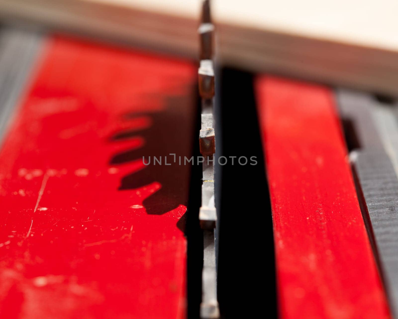 Focus on single carbide tooth of circular saw blade with a piece of plywood out of focus