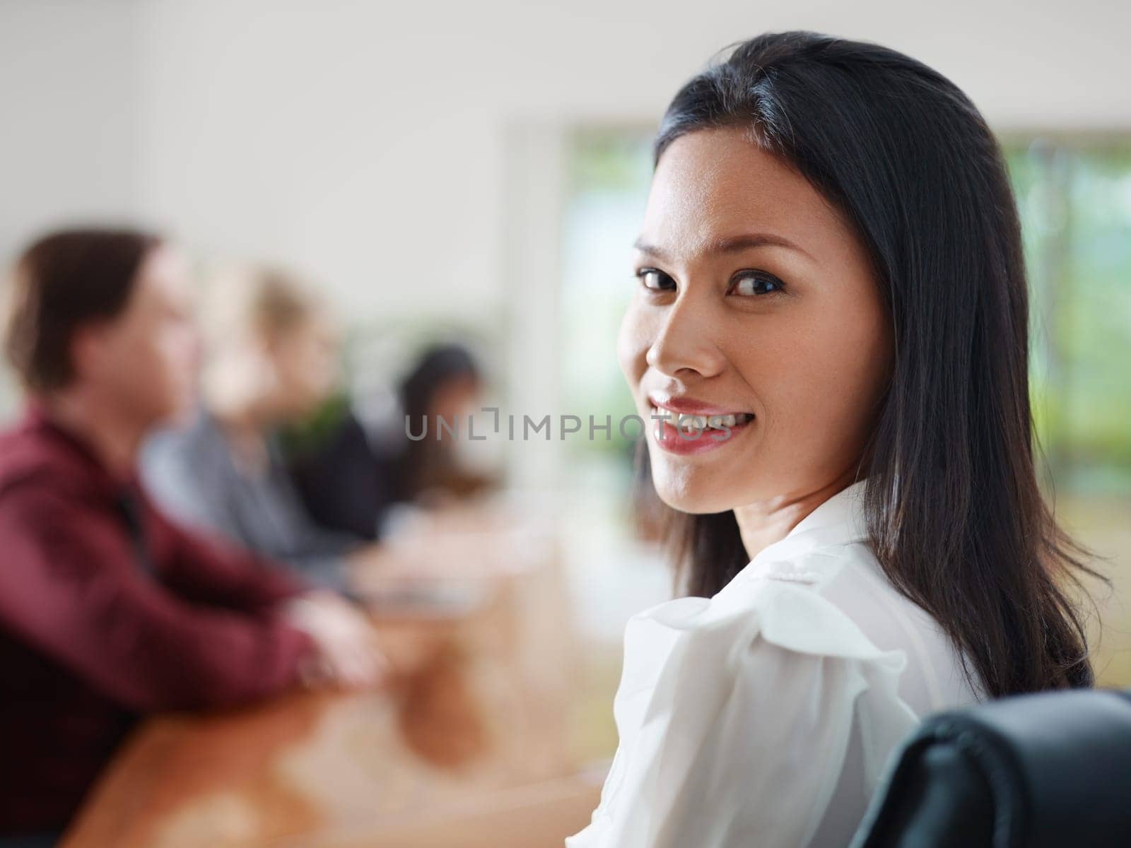 Attractive young Asian business woman smiling and looking over shoulders at business meeting with co-workers.