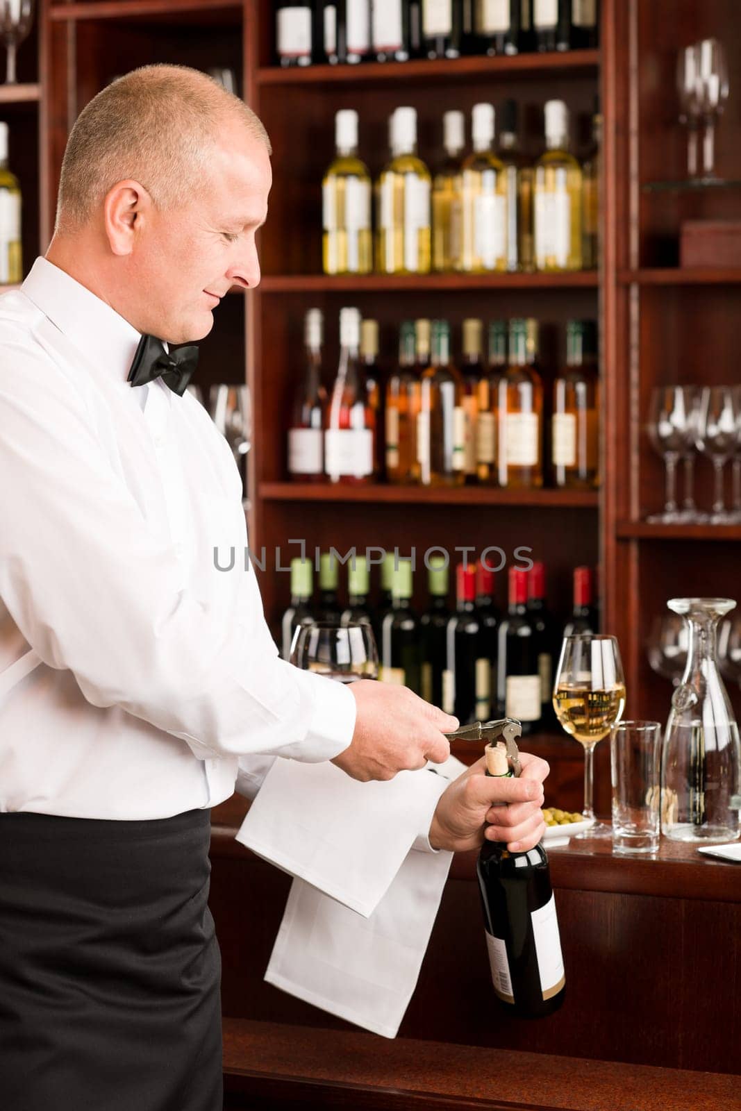 Wine bar professional waiter mature opening bottle in restaurant