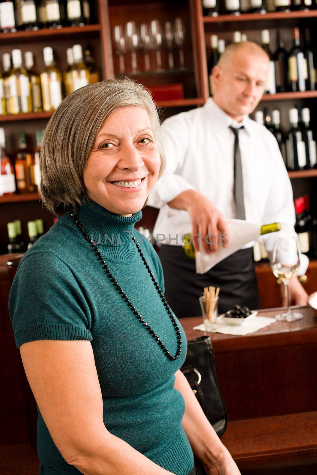 Wine bar senior woman enjoy wine glass in front of bartender