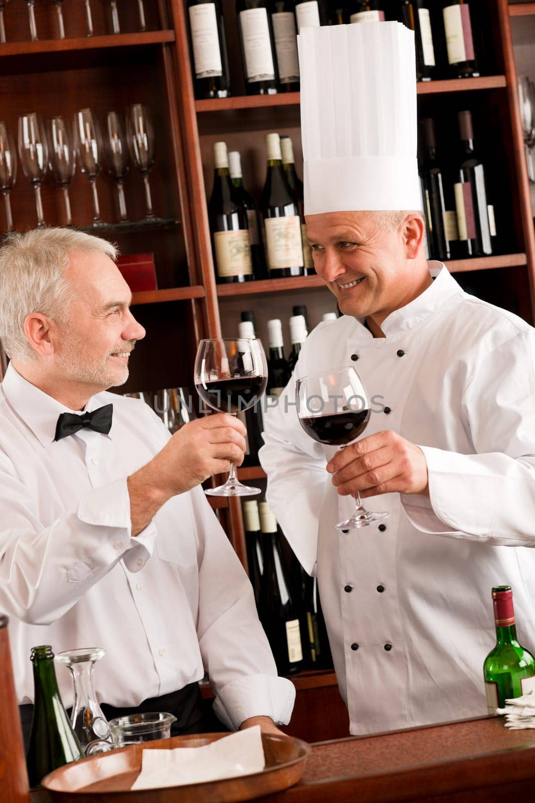 Chef cook and waiter toasting with wine smiling in restaurant