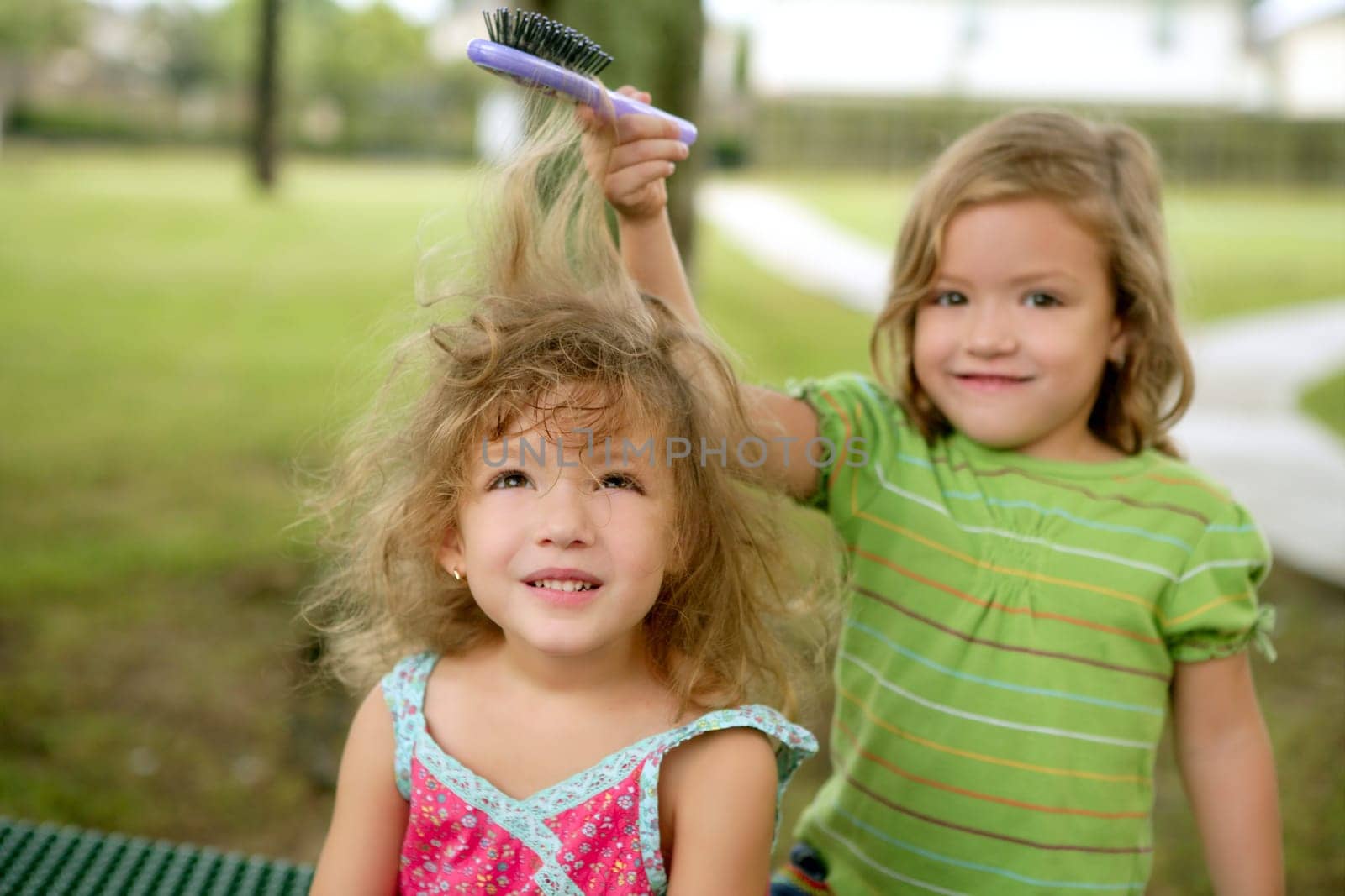 Two twin little sisters pretending to be hairdresser outdoor