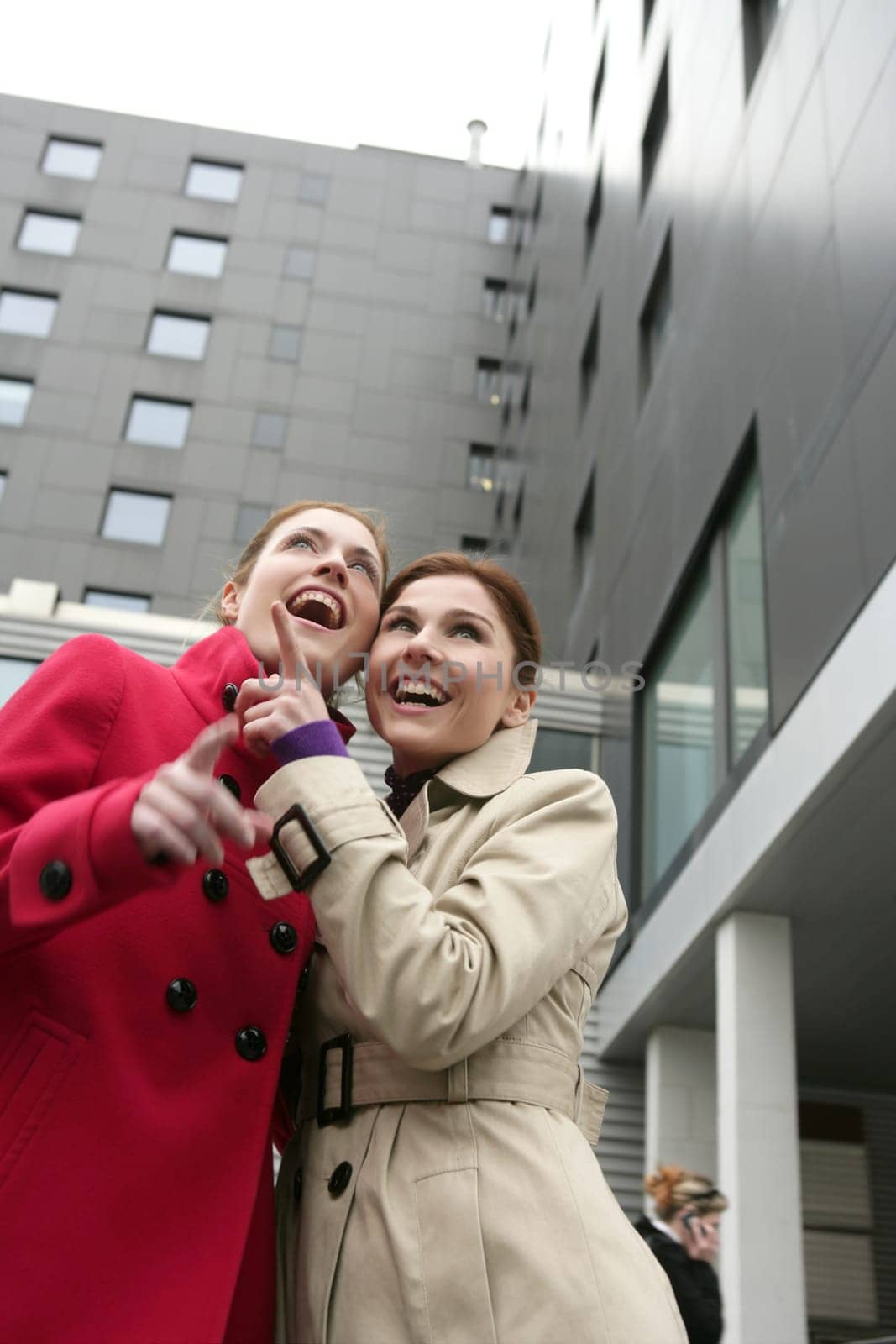 Two happy young women with winter coats, black building background
