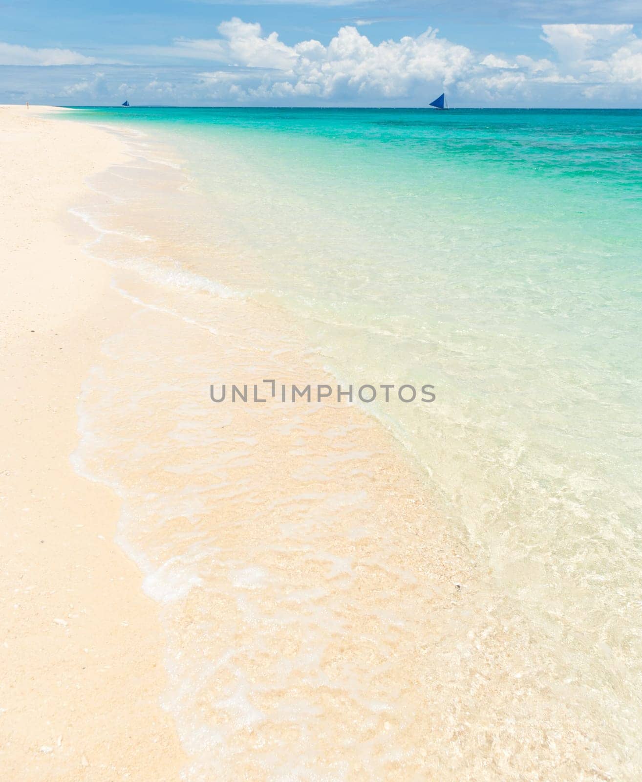 tropical white beach with a sailing boat at the horizon