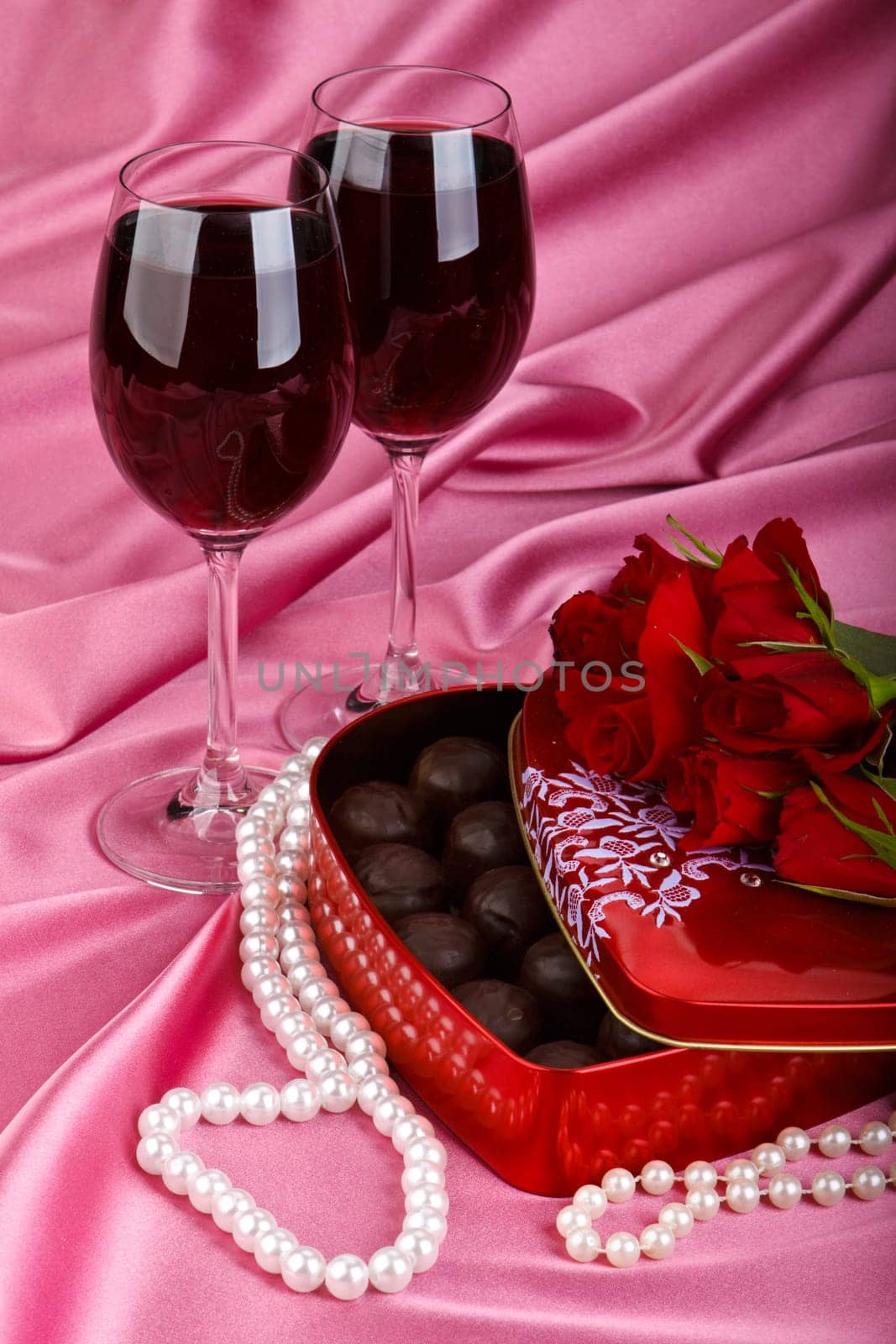 Heart-shaped red box with sweets, two glasses of red wine and bunch of flowers. Valentine&#039 s day card.