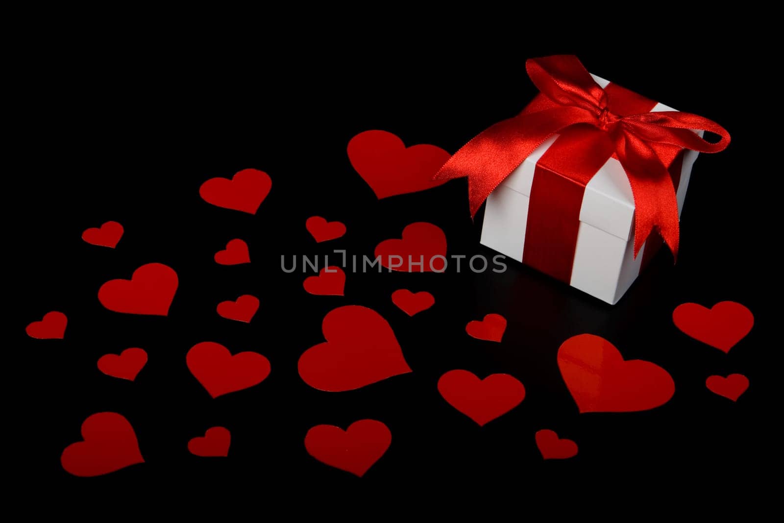 Gift box and red hearts on a black background. Valentine&#039 s day card.