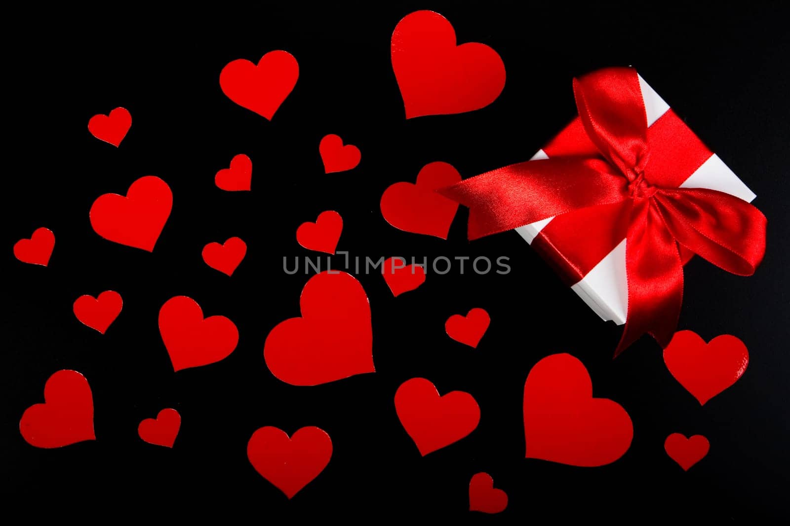 Gift box and red hearts on a black background. Valentine&#039 s day card.