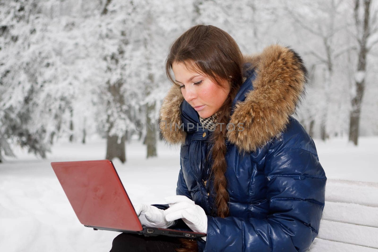 The beautiful girl with the laptop sits on a bench in winter park.