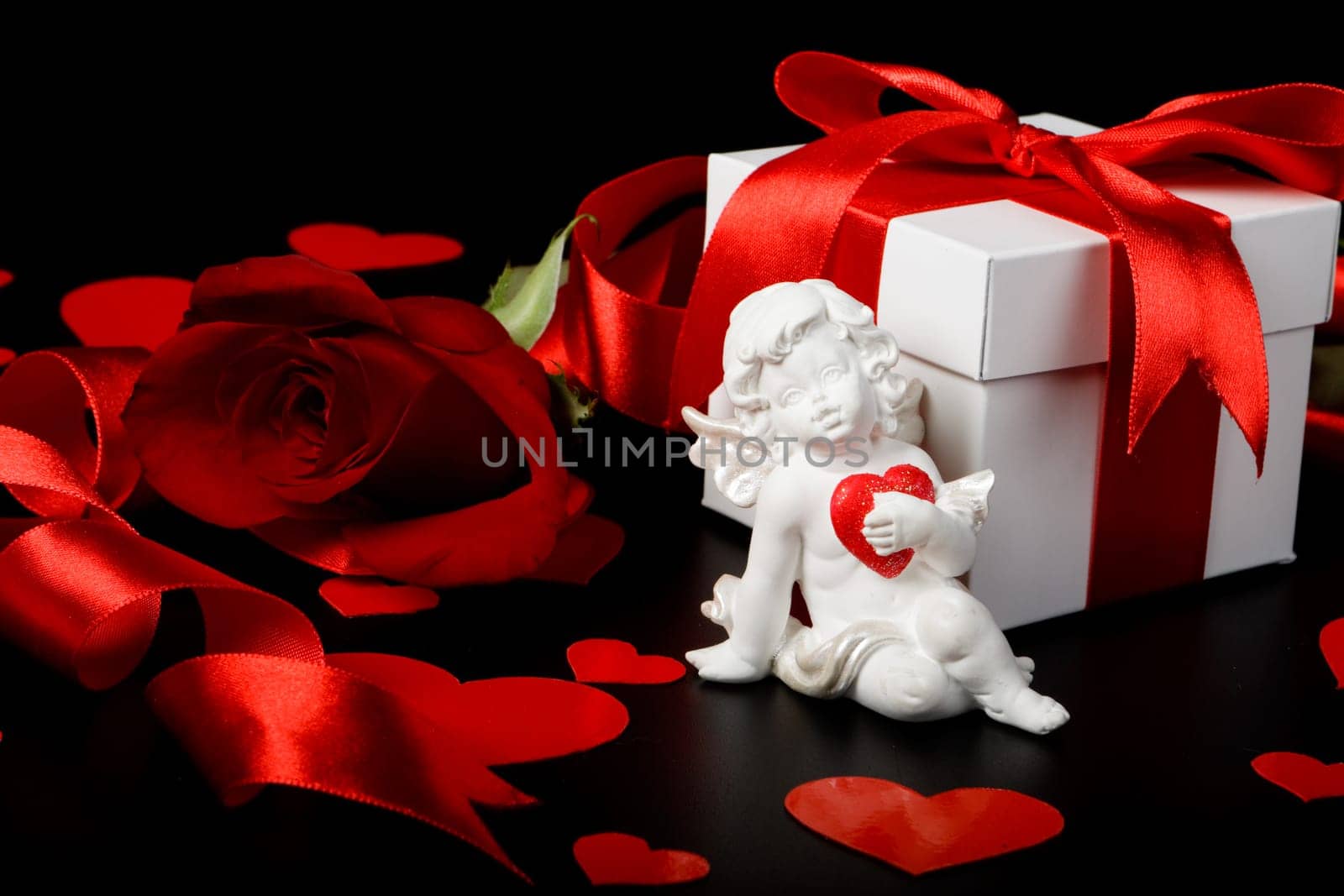Gift box, cupid, red hearts and rose on a black background. Valentine&#039 s day card.
