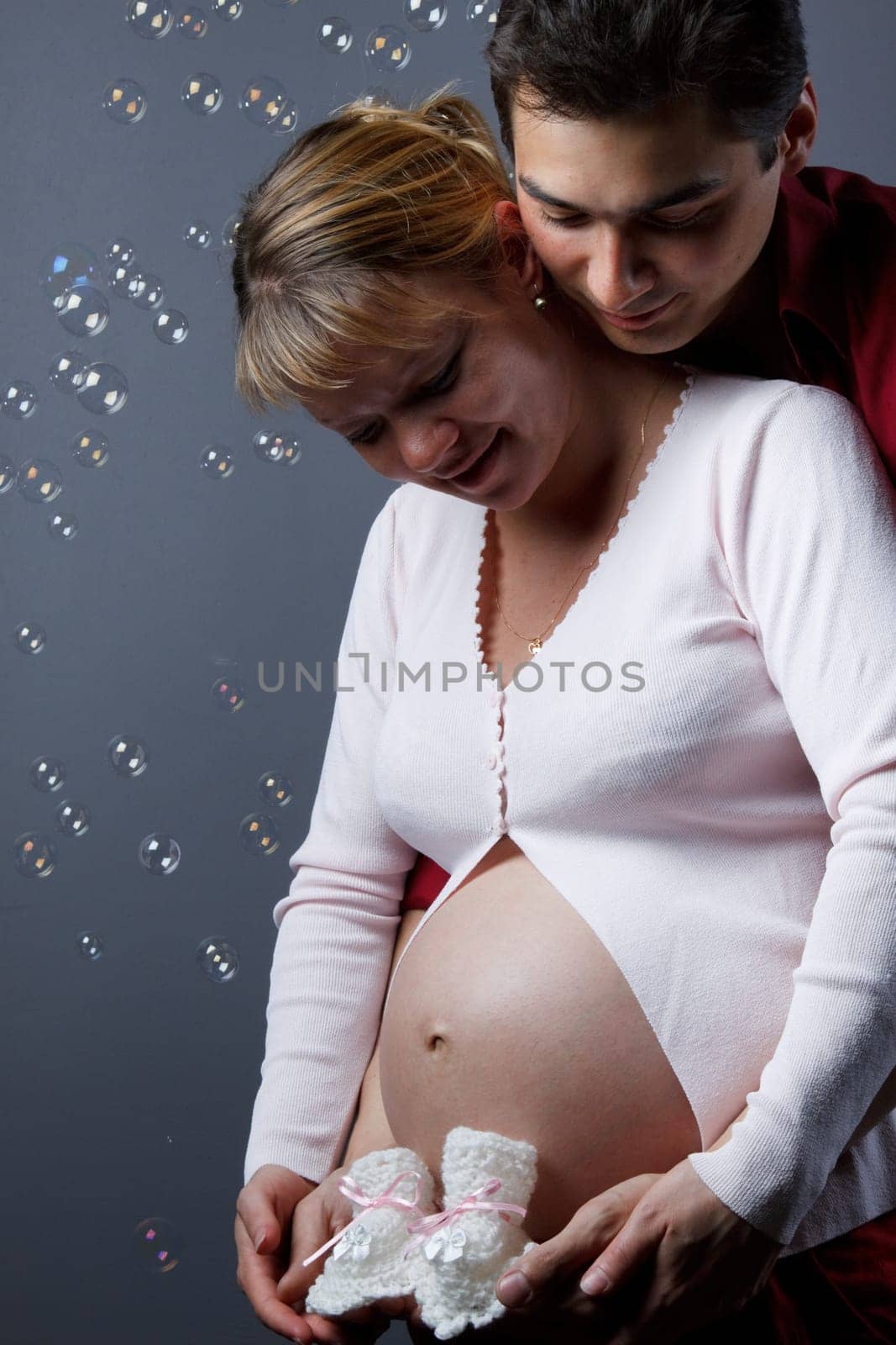 The young family expecting a birth of the child, holds bootees on a grey background