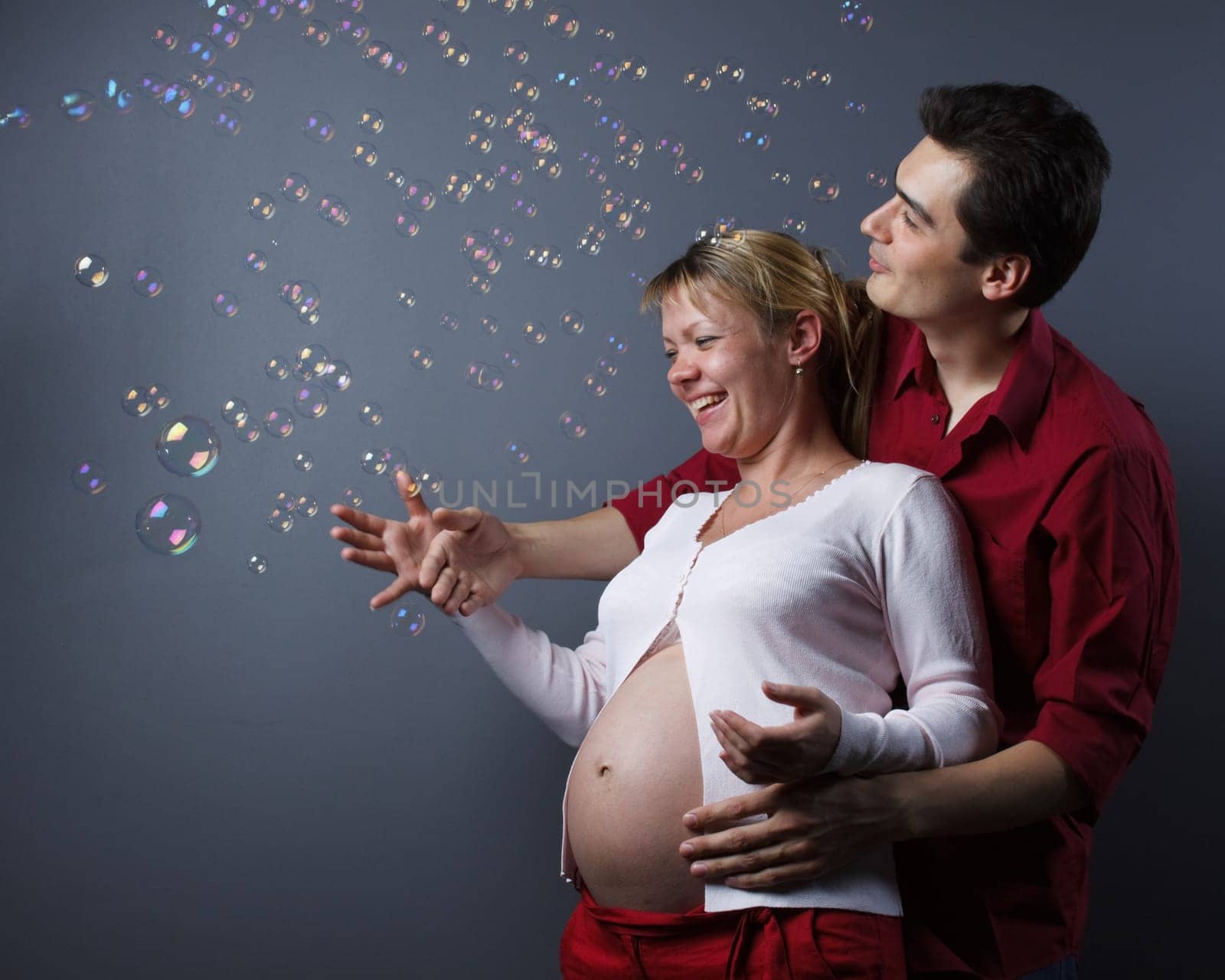 Happy beautiful pregnant woman and her husband catches soap bubbles