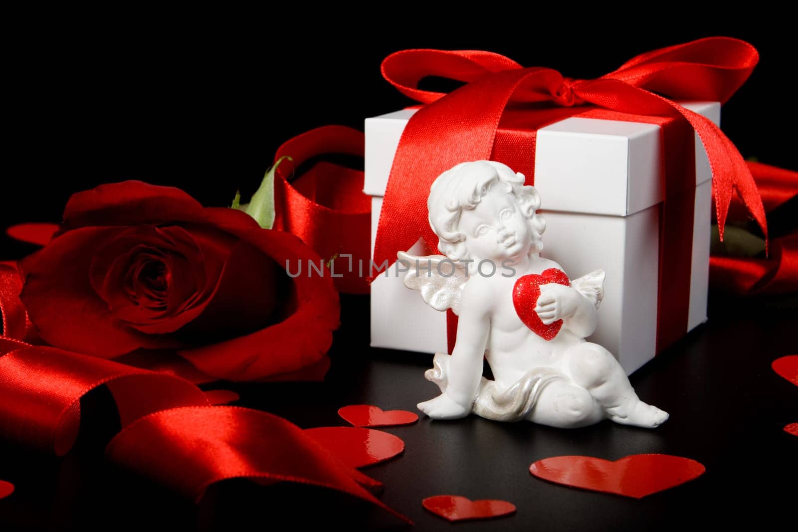 Gift box, cupid, red hearts and rose on a black background. Valentine&#039 s day card.