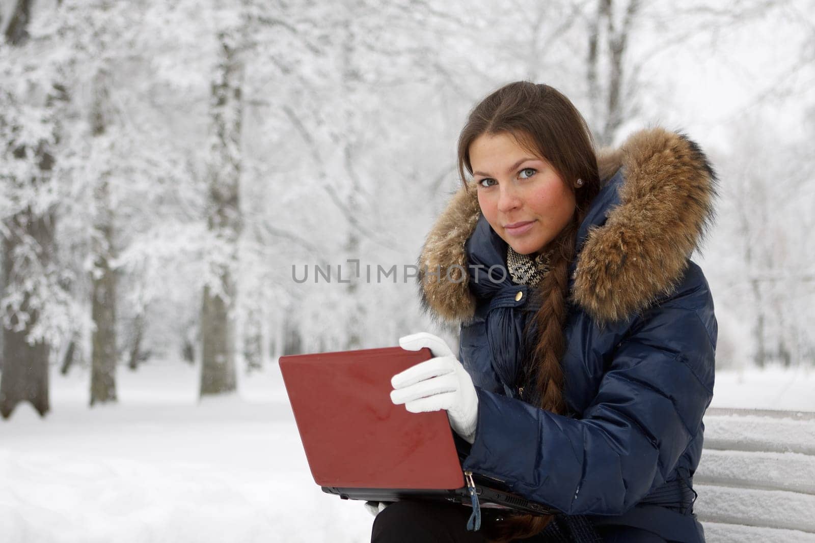 The beautiful girl with the laptop sits on a bench in winter park.