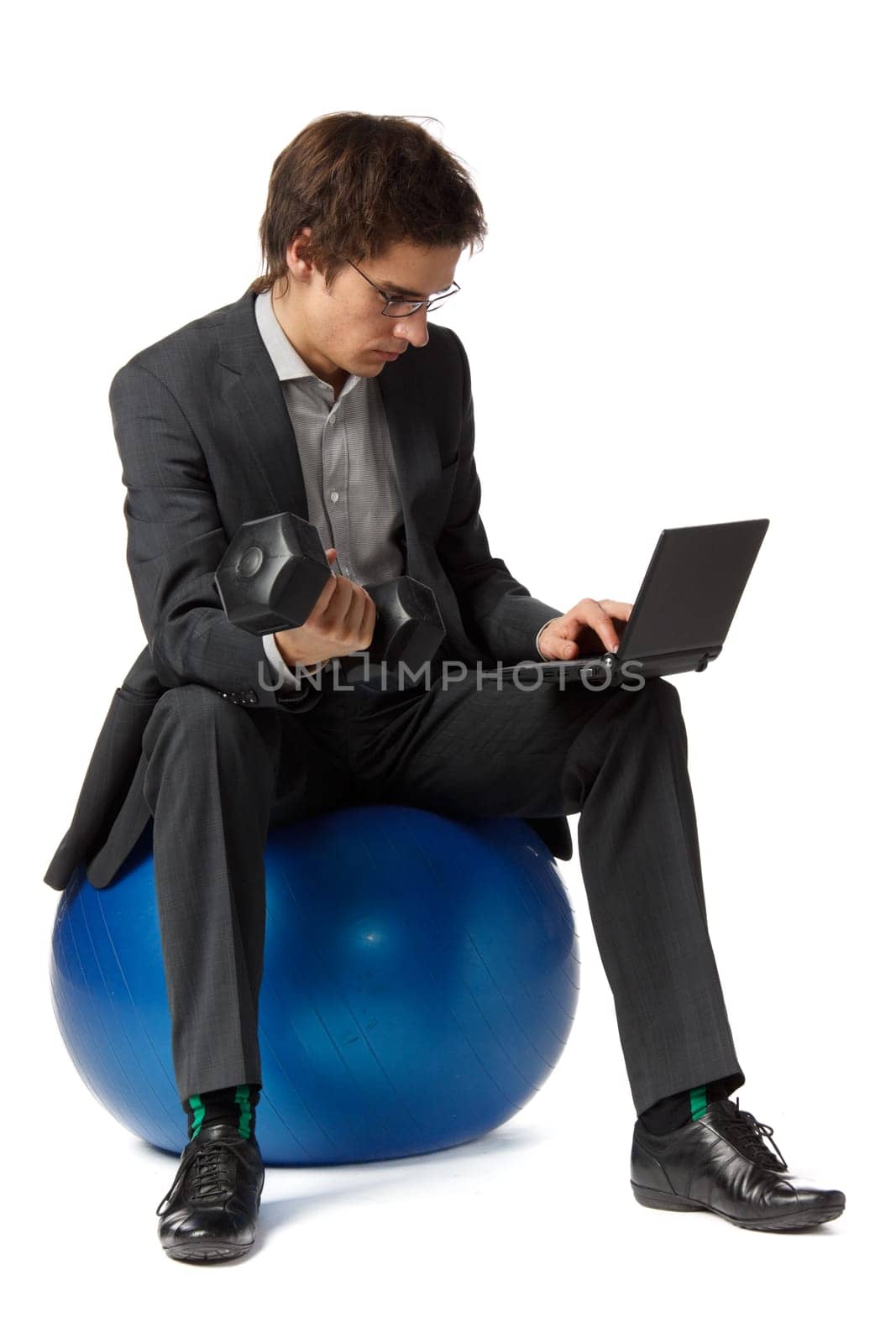 The young businessman simultaneously works on the computer and and does exercise with dumbbells.