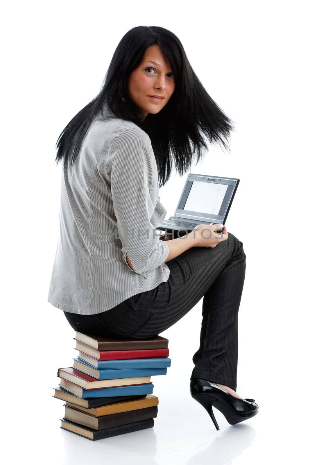The attractive student sits on a pile of books with the laptop on a white background.
