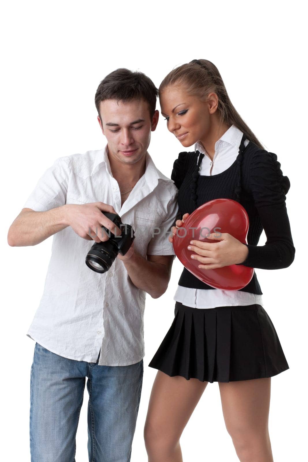 The girl with a red heart and the young man examine photos on a camera on a white background.
