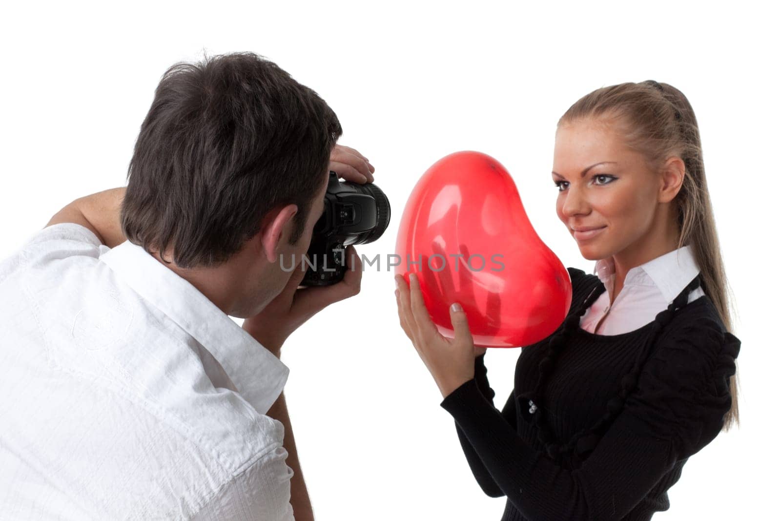 The beautiful girl with a red heart poses for the young guy on a white background. Selective focus on photographer.