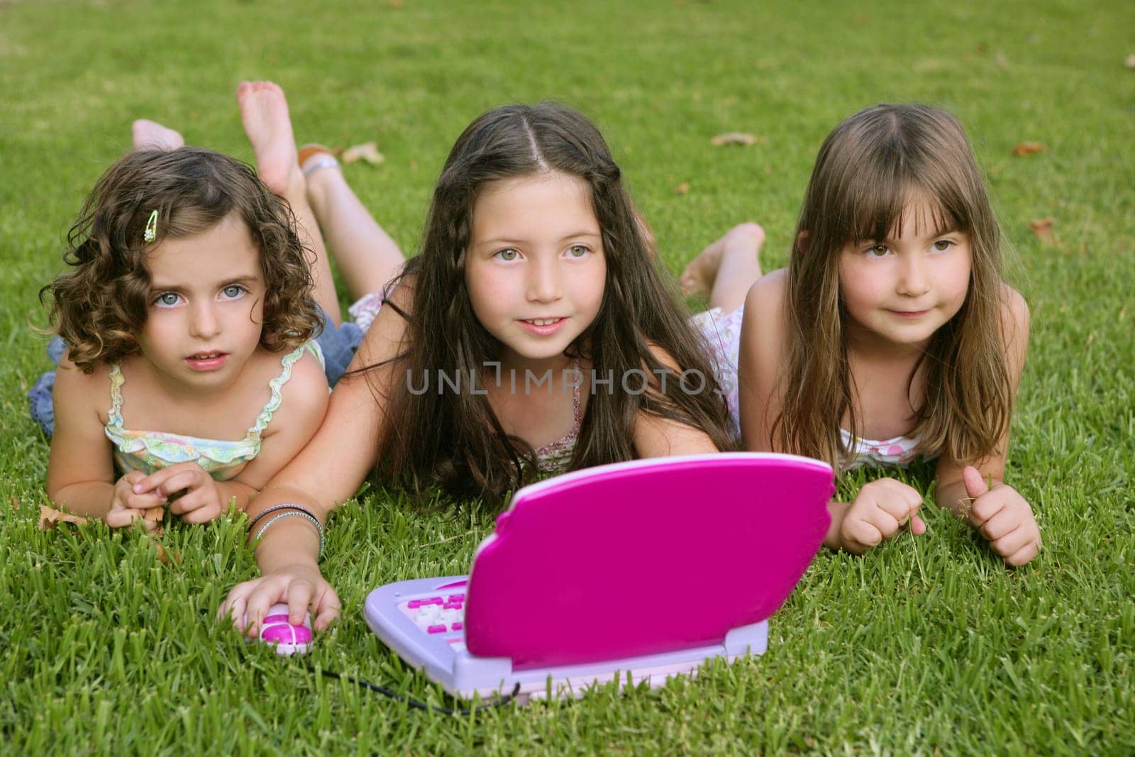 Three little girl outdoor playing with toy computer in grass