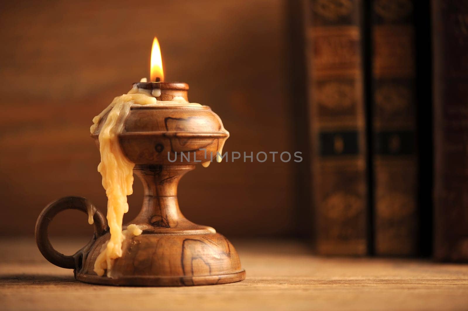 old candle on a wooden table, old books in the background