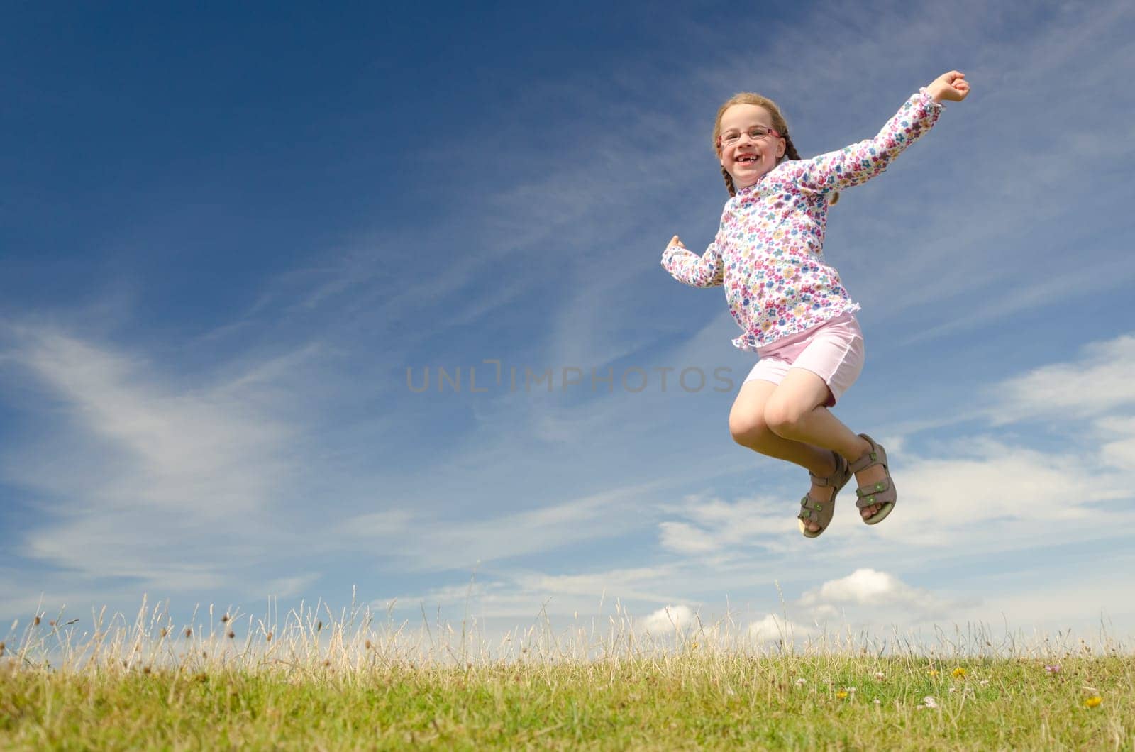 Young girl jumping on a green meadow against blue sky