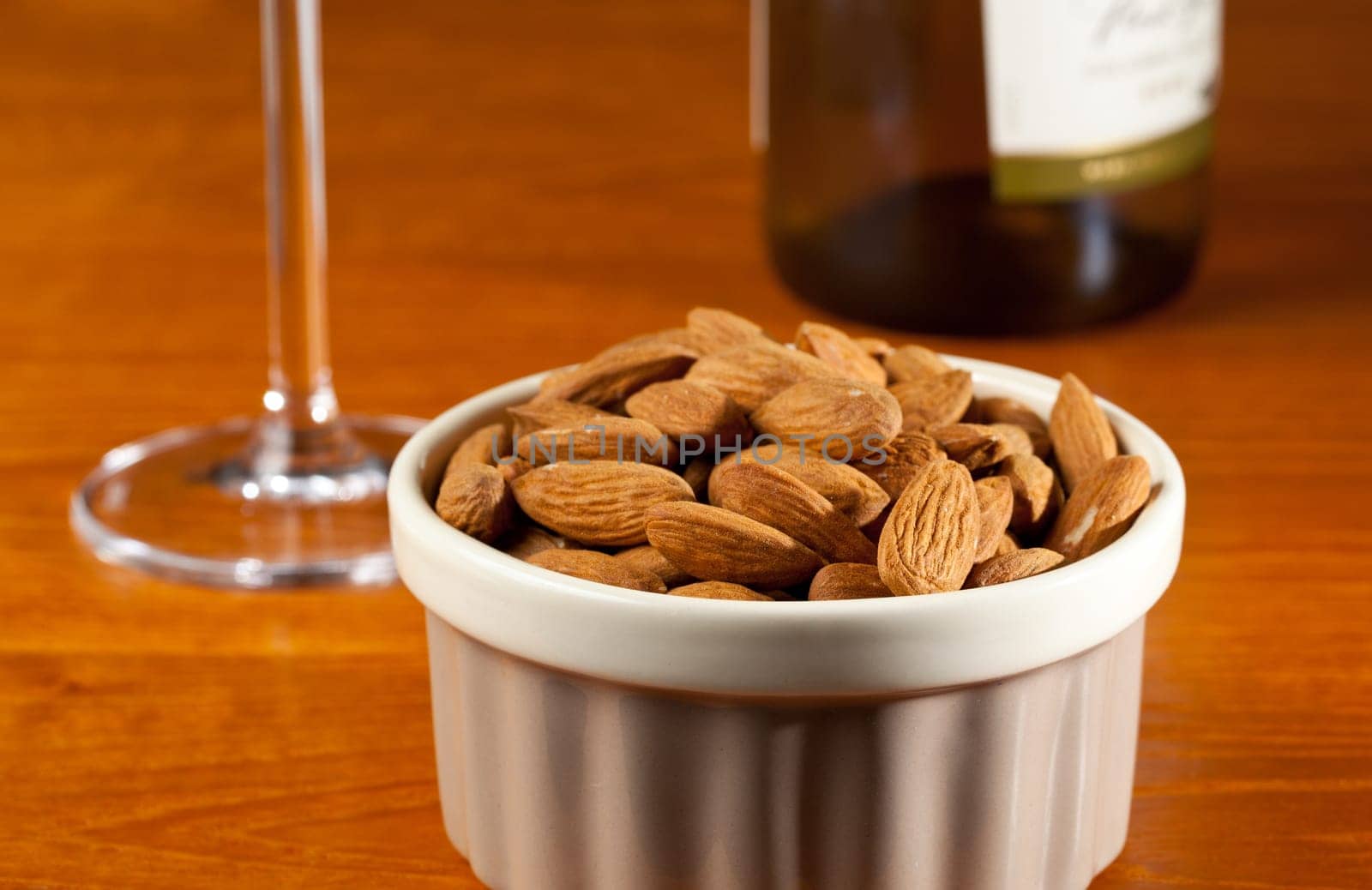 Pile of almond nuts in a porcelain bowl with glass and bottle of white wine