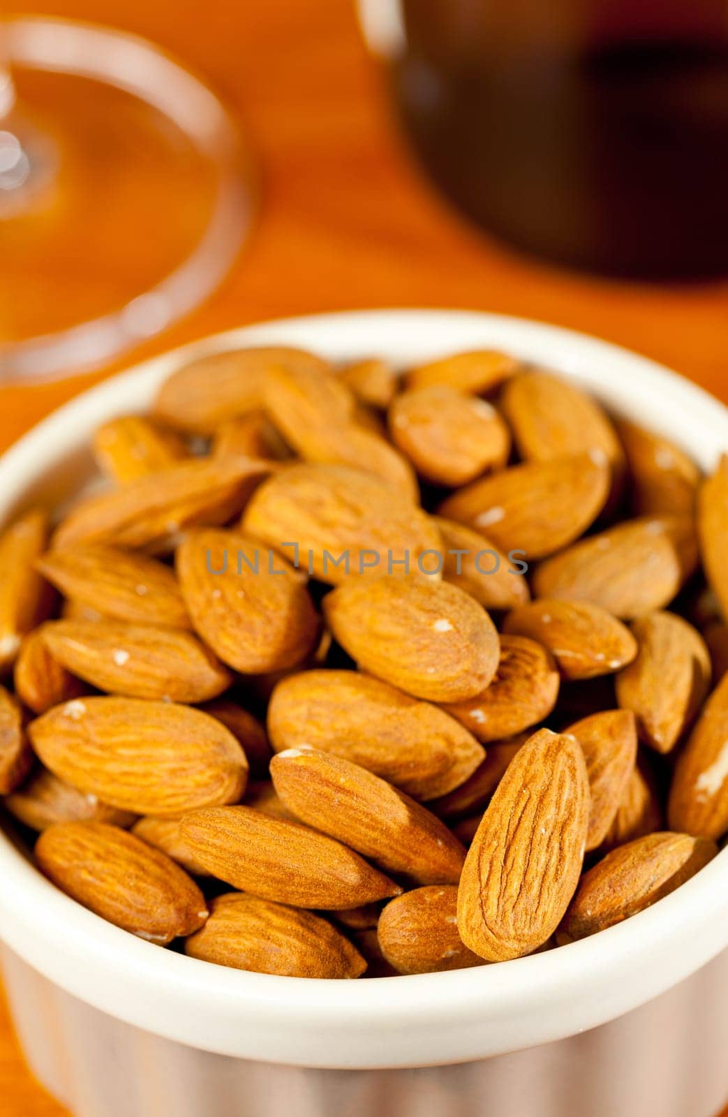 Pile of almond nuts in a porcelain bowl with glass and bottle of white wine