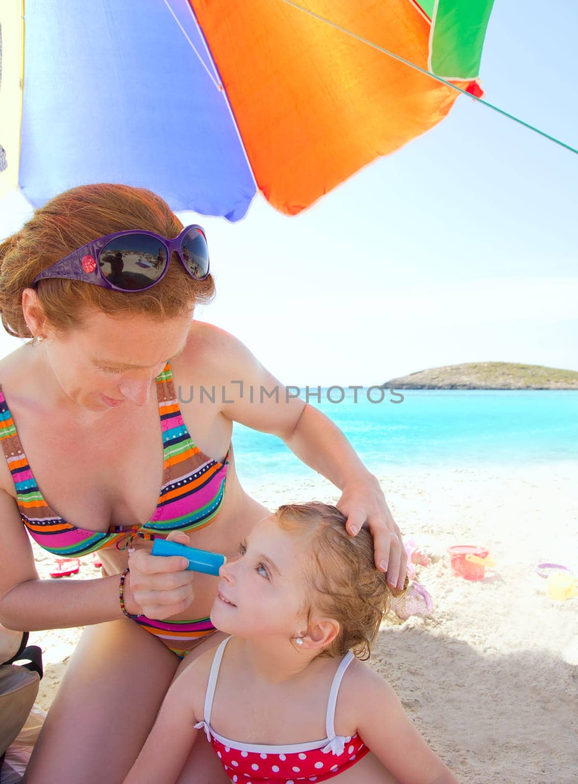 daughter and mother in beach with sunscreen in bikini