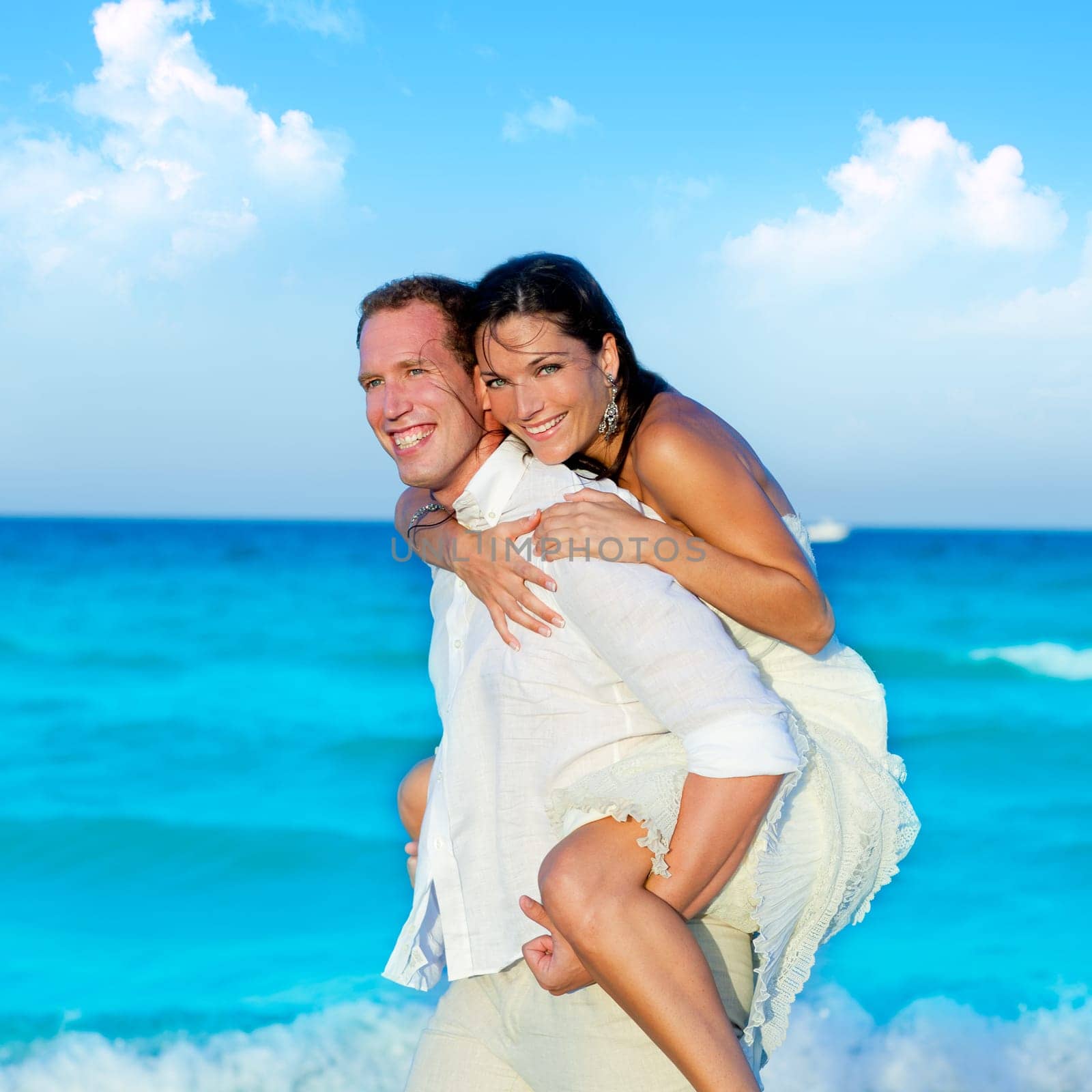 couple in love piggyback playing in a beach at blue Mediterranean