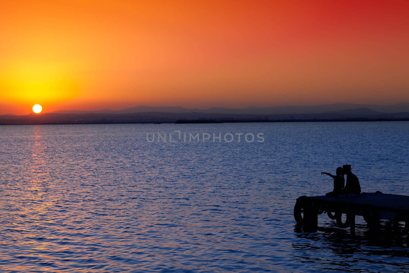 Mother and daughter in sunset jetty lake with orange sun
