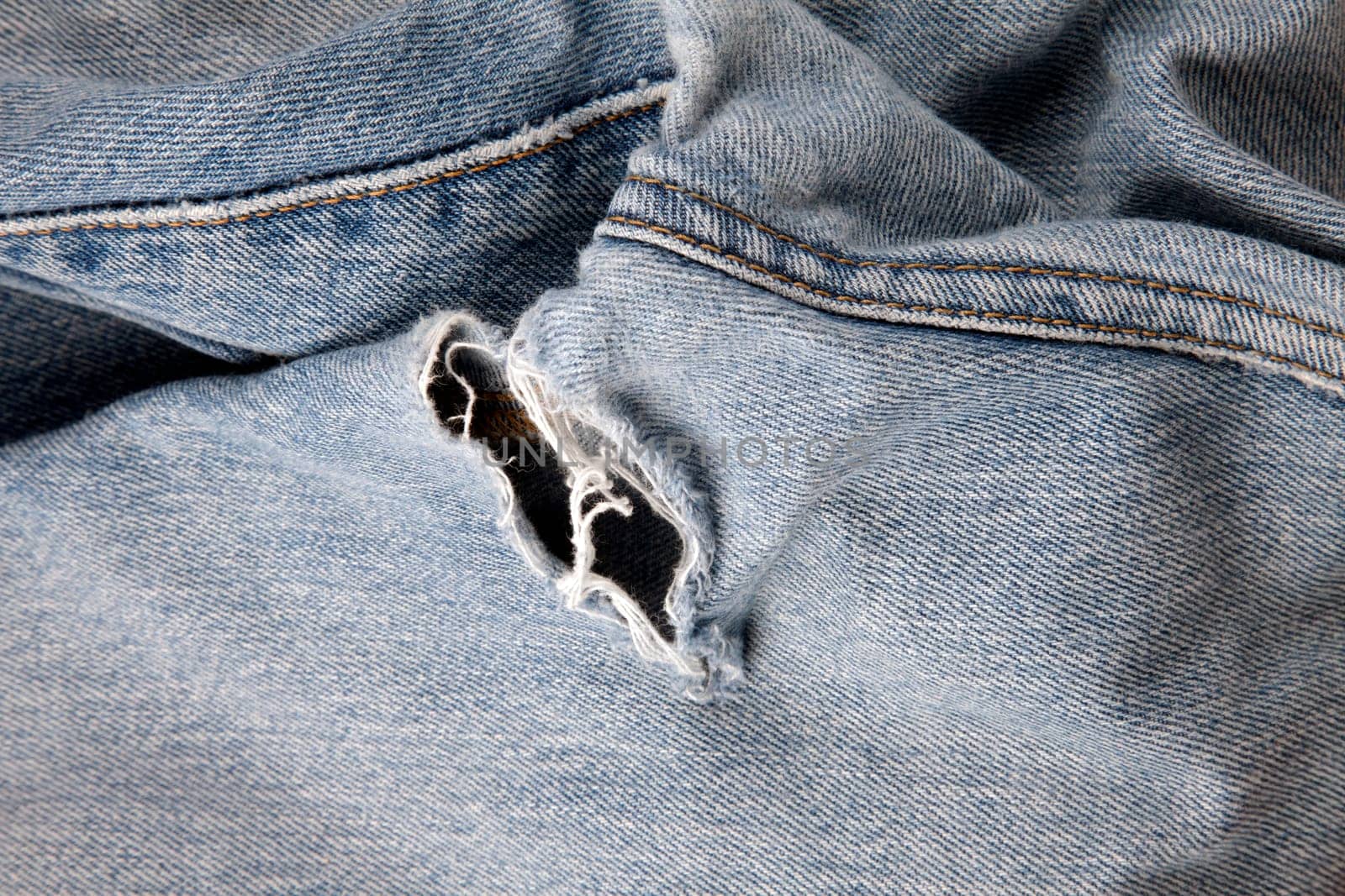 Close up of hole in an old pair of blue jeans showing the frayed threads.
