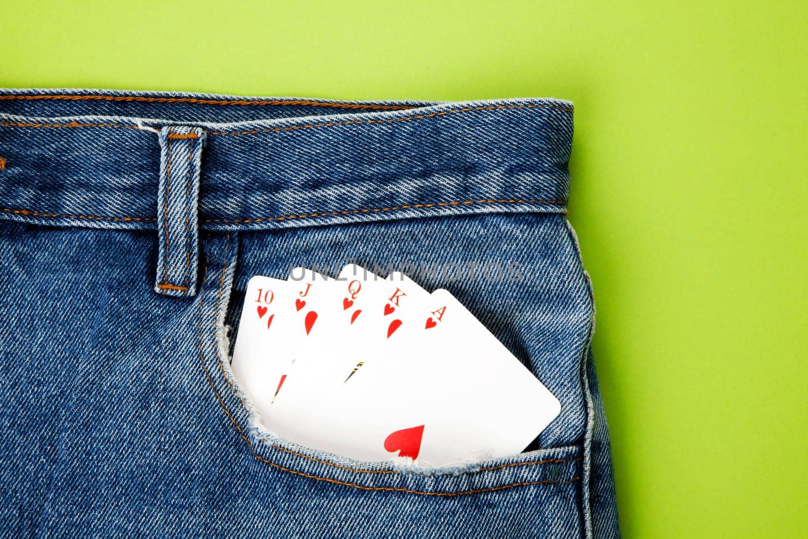 Royal flush with playing cards in blue jeans pocket with green background