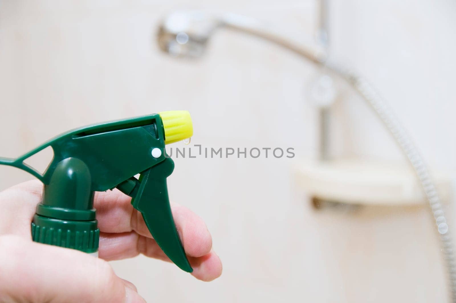 Hand with spray bottle in front of blurred handheld shower head in bright bathroom