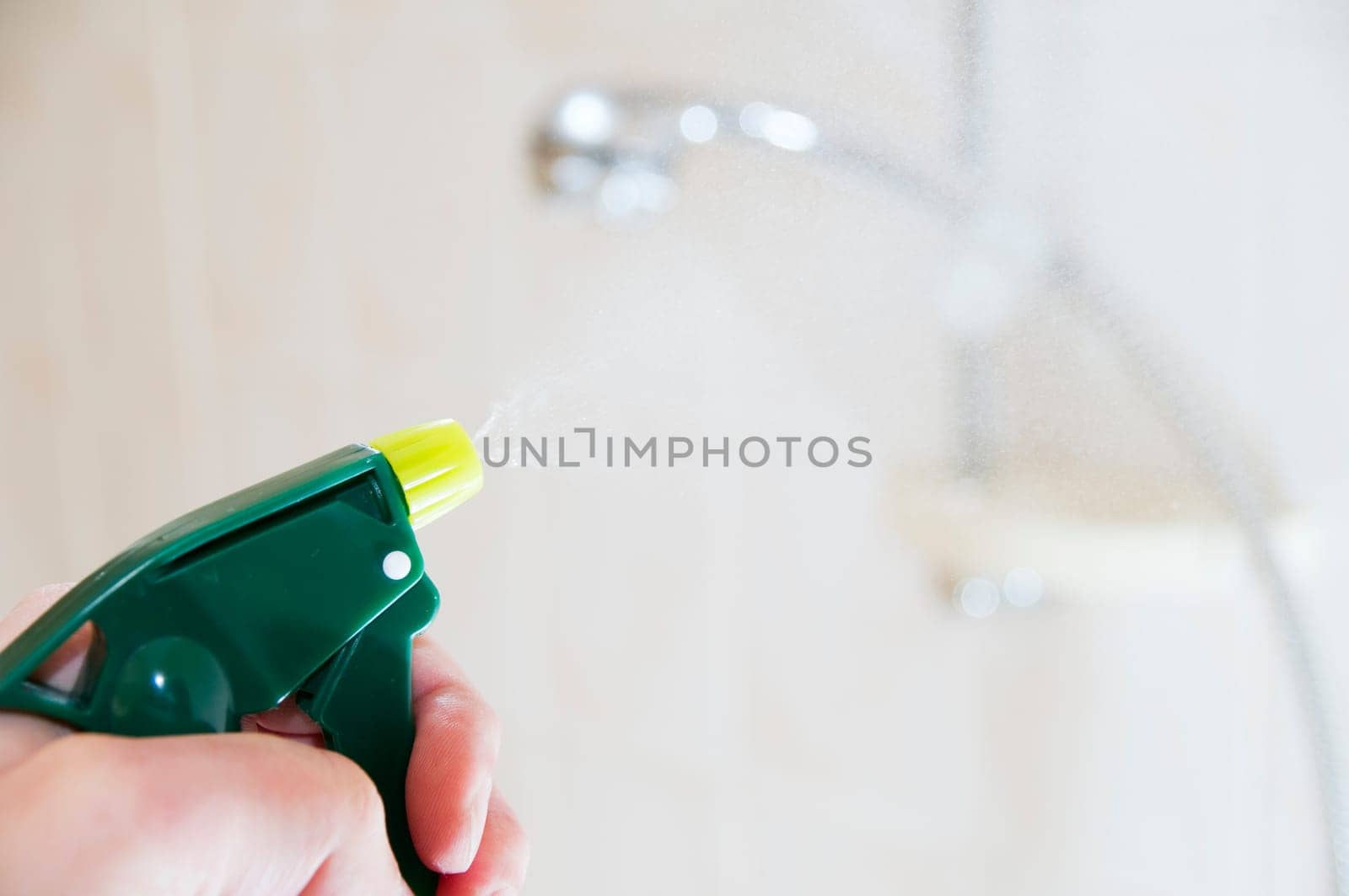 Hand with spray bottle in front of blurred handheld shower head in bright bathroom