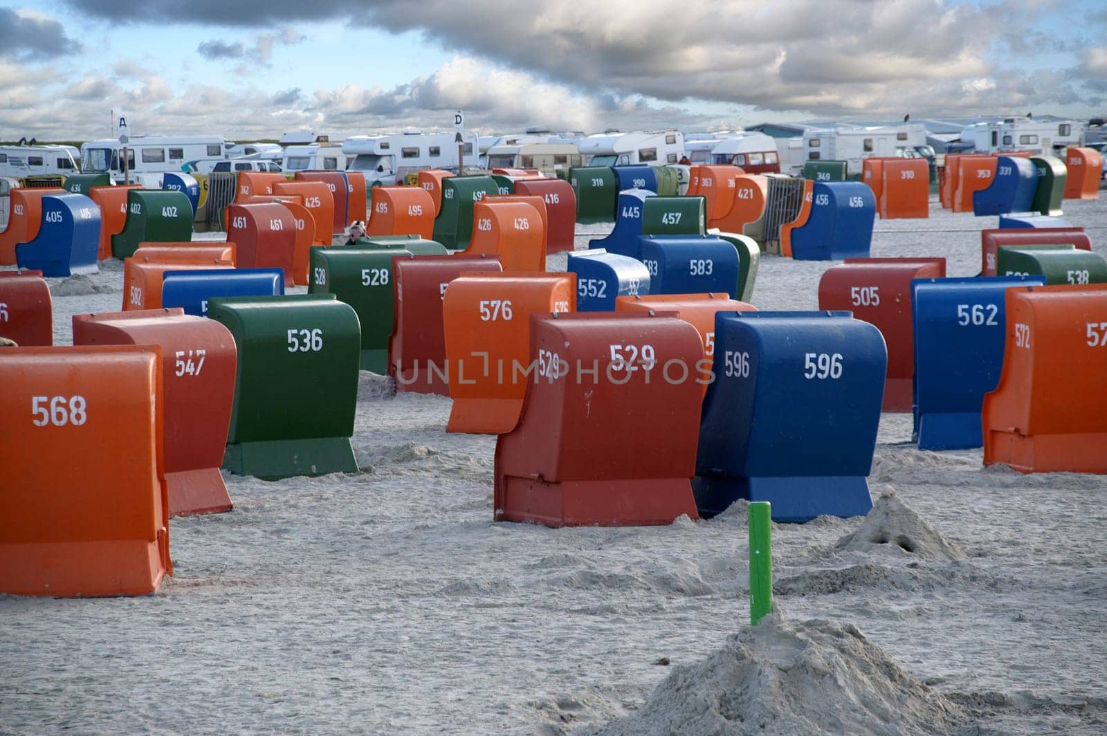 Beach chairs on the North Sea beach with cloudy sky and motorhomes in the background