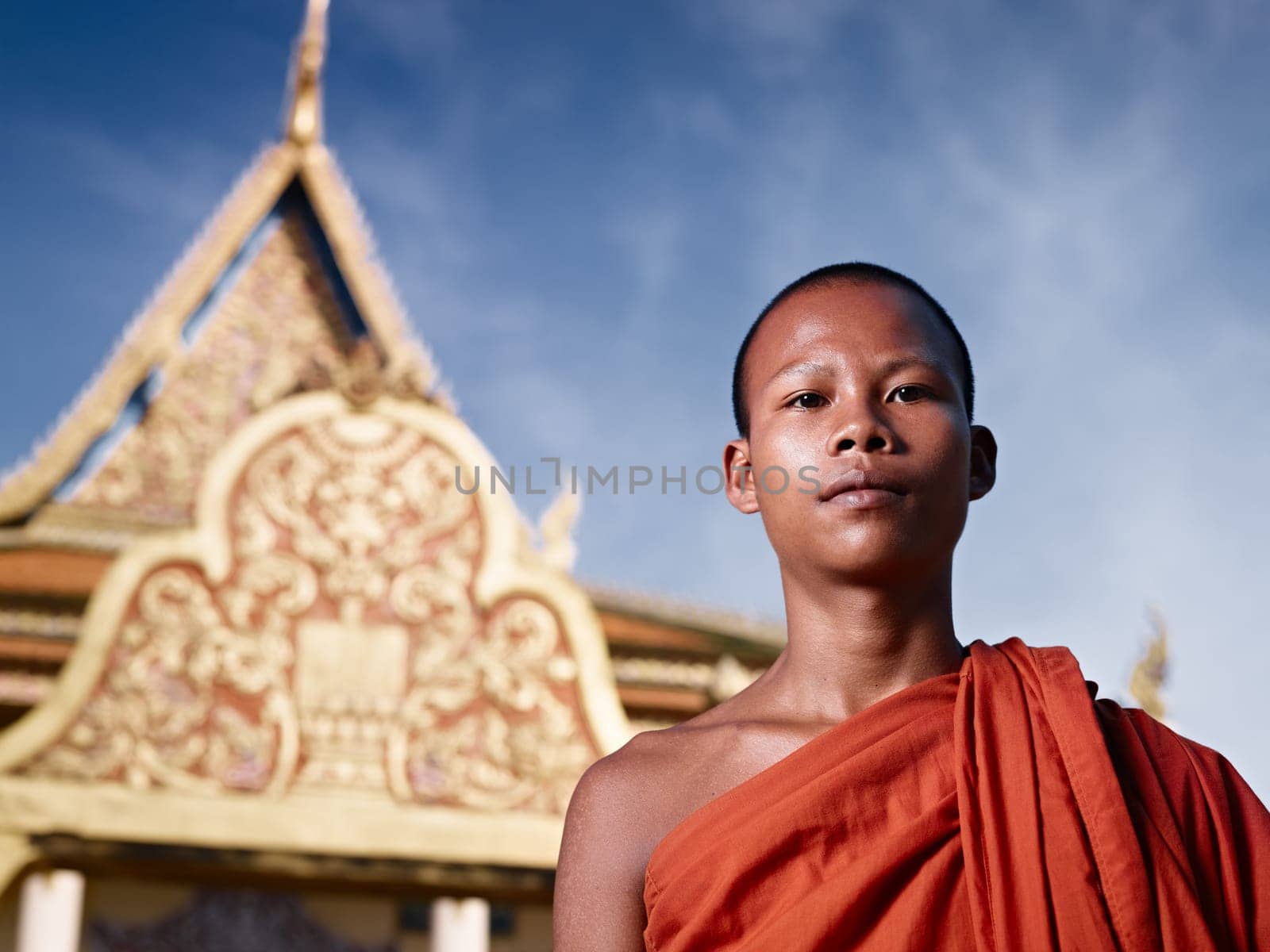 Young Asian monk smiling at camera in buddhist monastery, Phnom Penh, Cambodia, Asia. Low angle