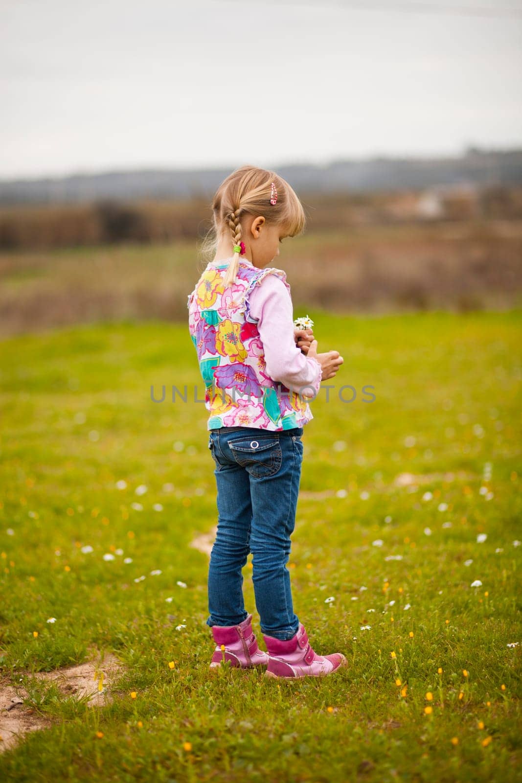Cute little girl standing on a green field with flowers
