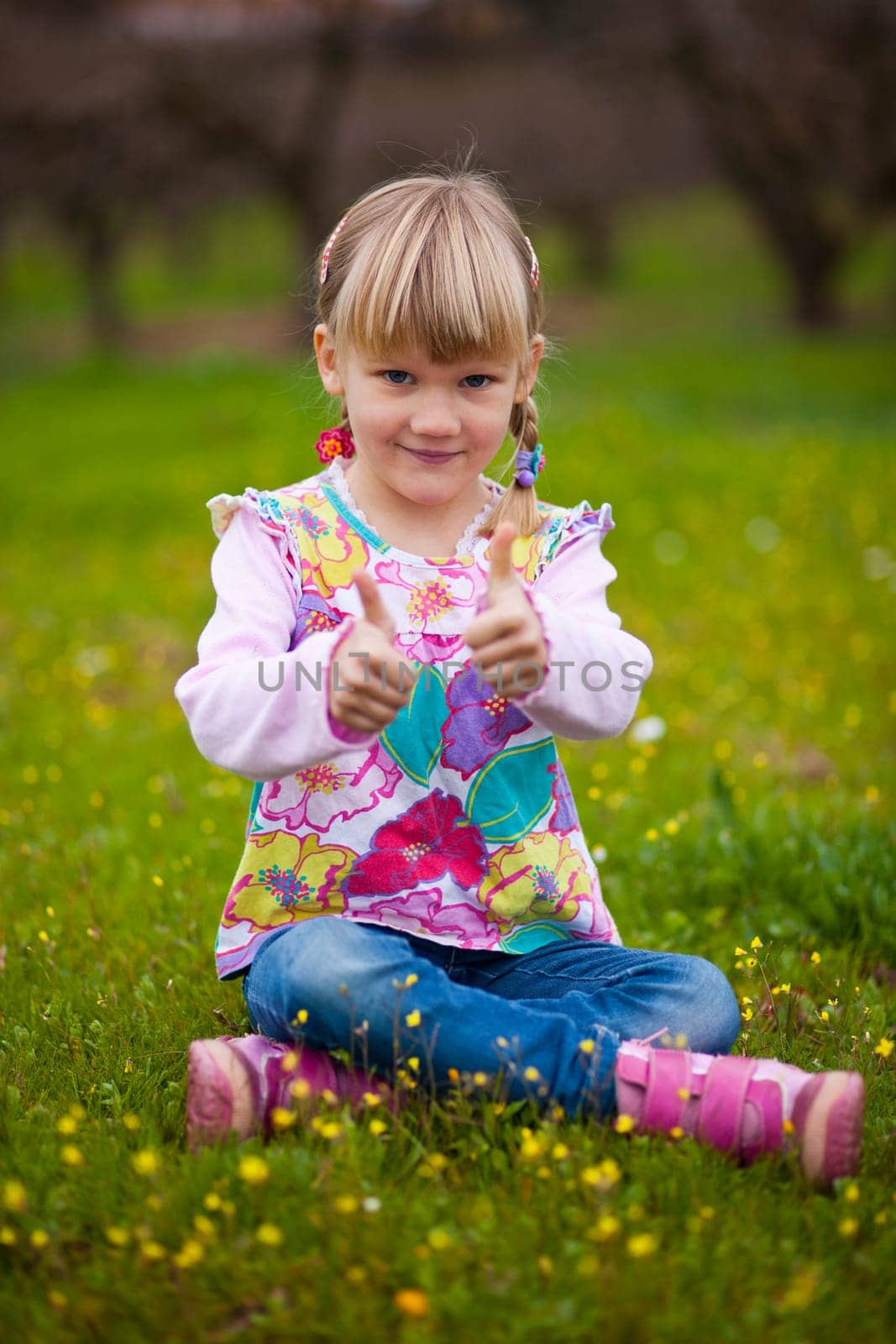 Cute little girl outdoors on a green field with thumbs up