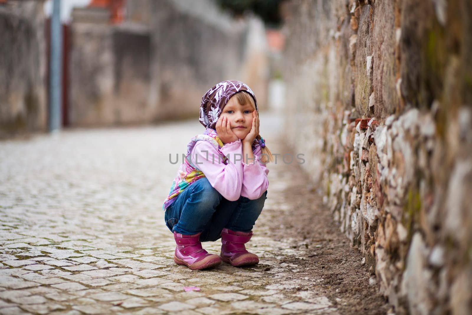 Portrait of a little girl outdoors on a city street, hands on cheeks