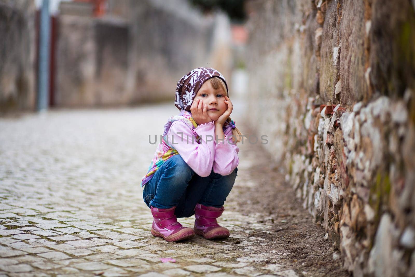 Portrait of a little girl outdoors on a city street, hands on cheeks