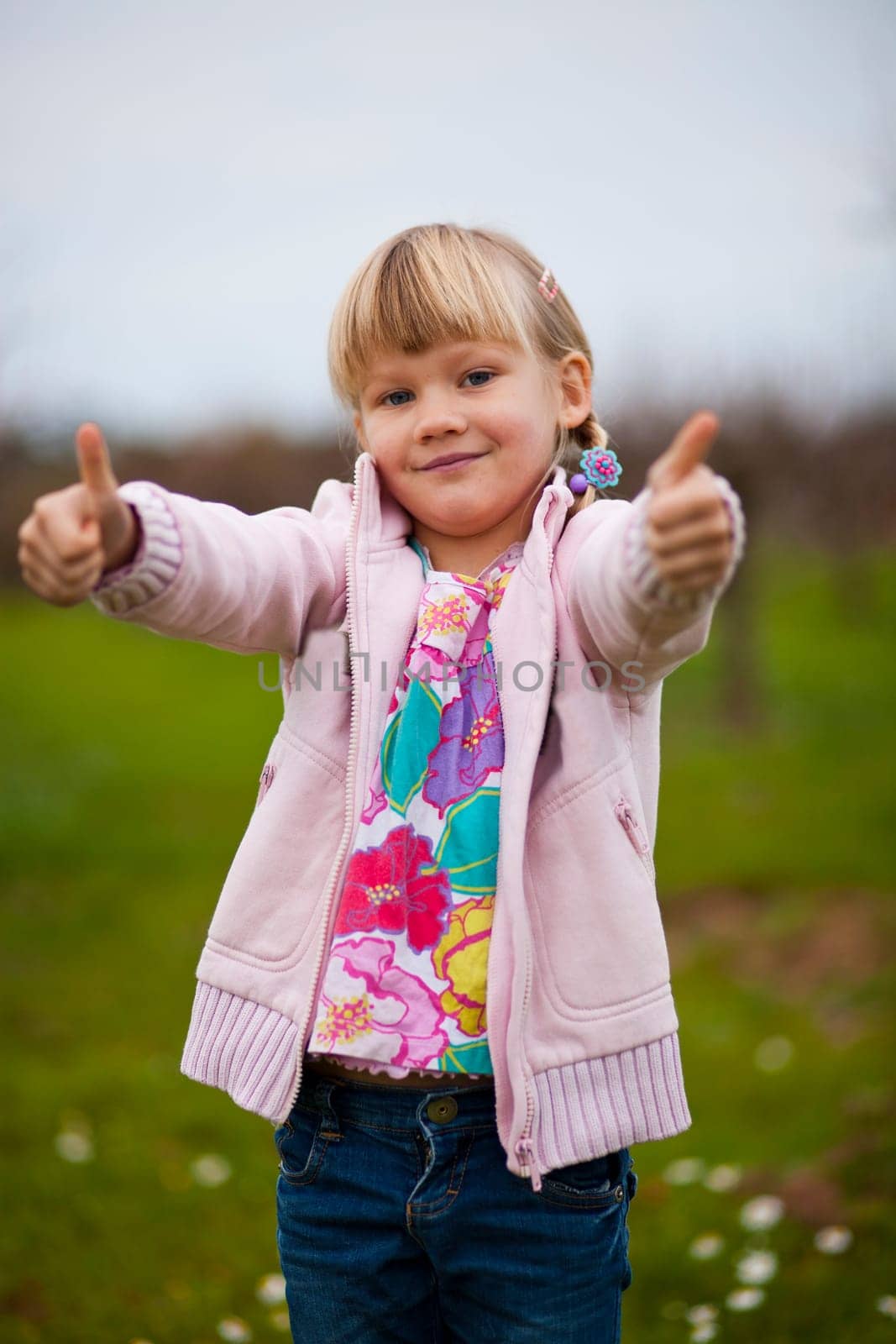 Cute little girl outdoors on a green field with thumbs up