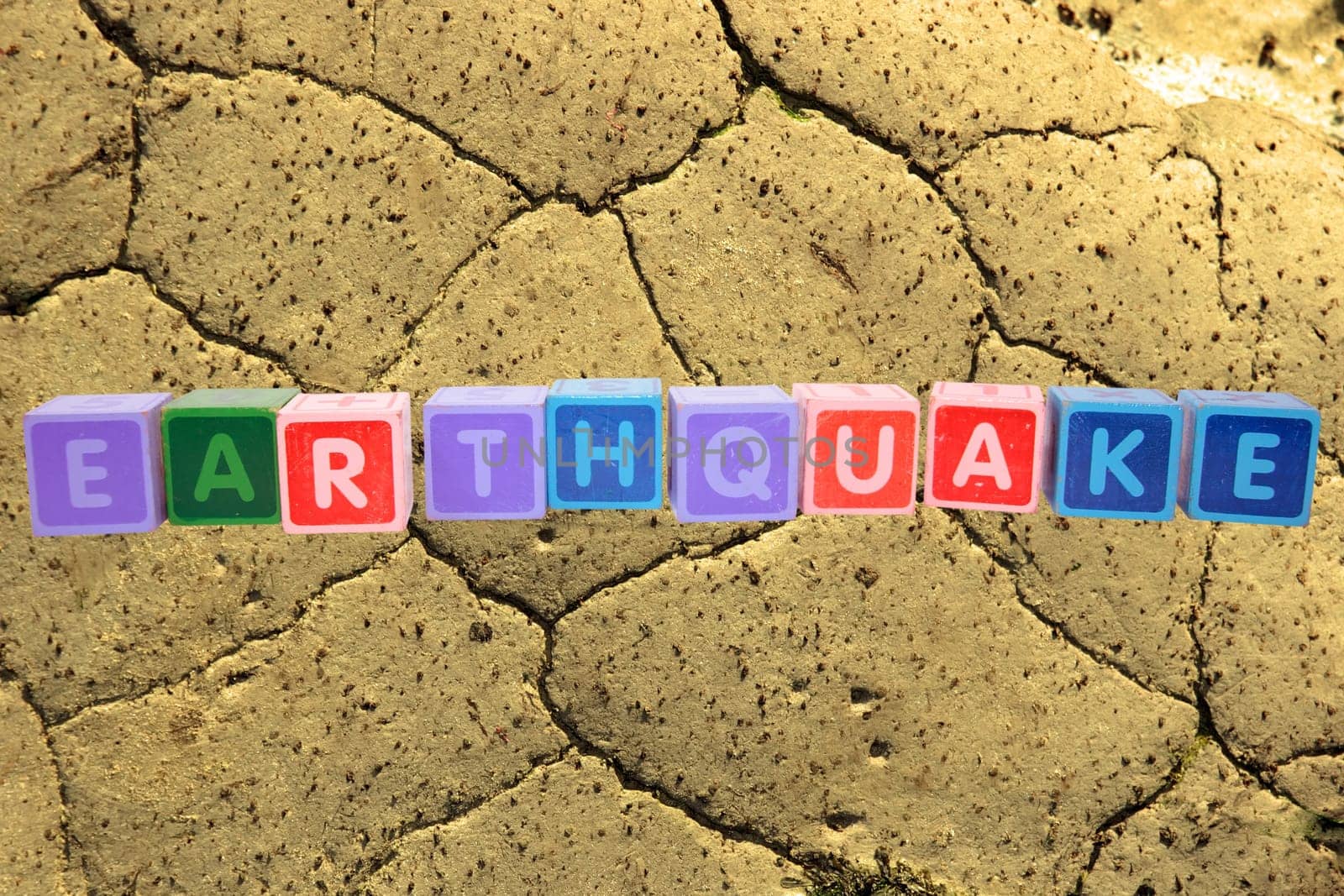 toy letters that spell earthquake against a barren land background with clipping path
