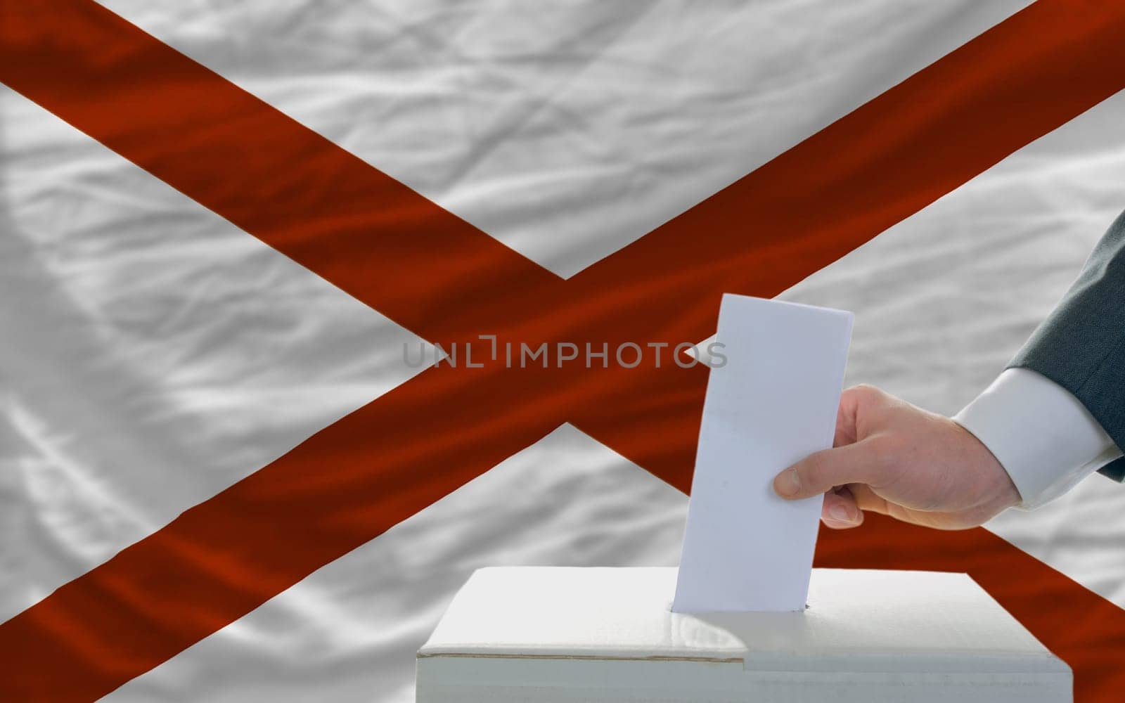 man putting ballot in a box during elections  in front of flag american state of alabama