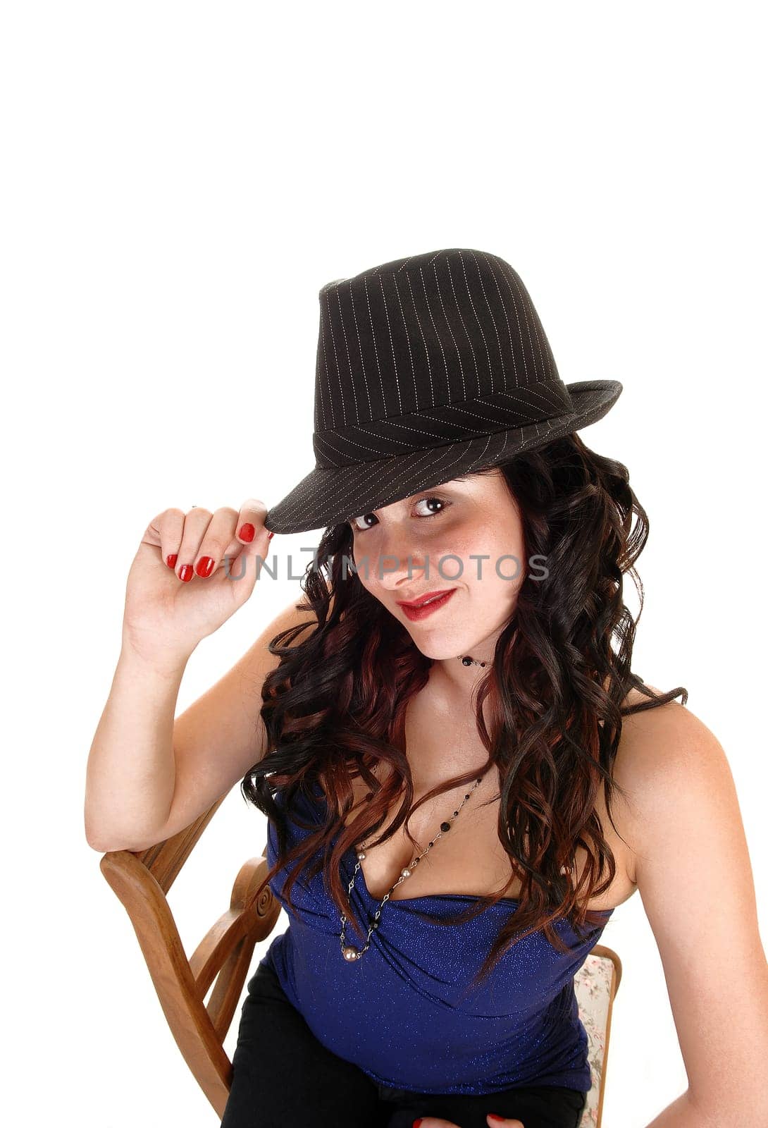 Young pretty woman with a gray hat and long black curly hair sitting on a chair, looking smiling into the camera, for white background.