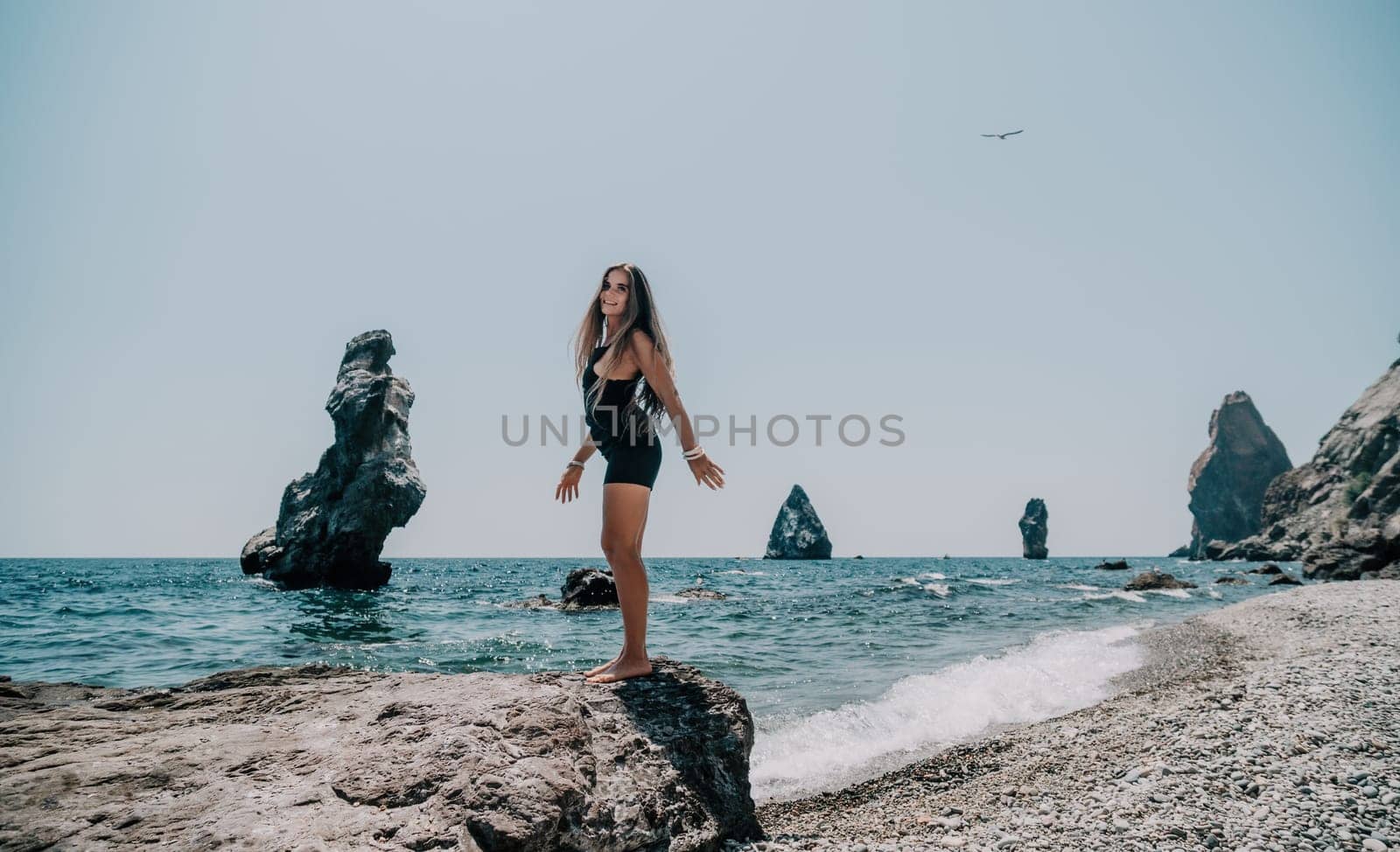 Woman travel sea. Young Happy woman in a long red dress posing on a beach near the sea on background of volcanic rocks, like in Iceland, sharing travel adventure journey