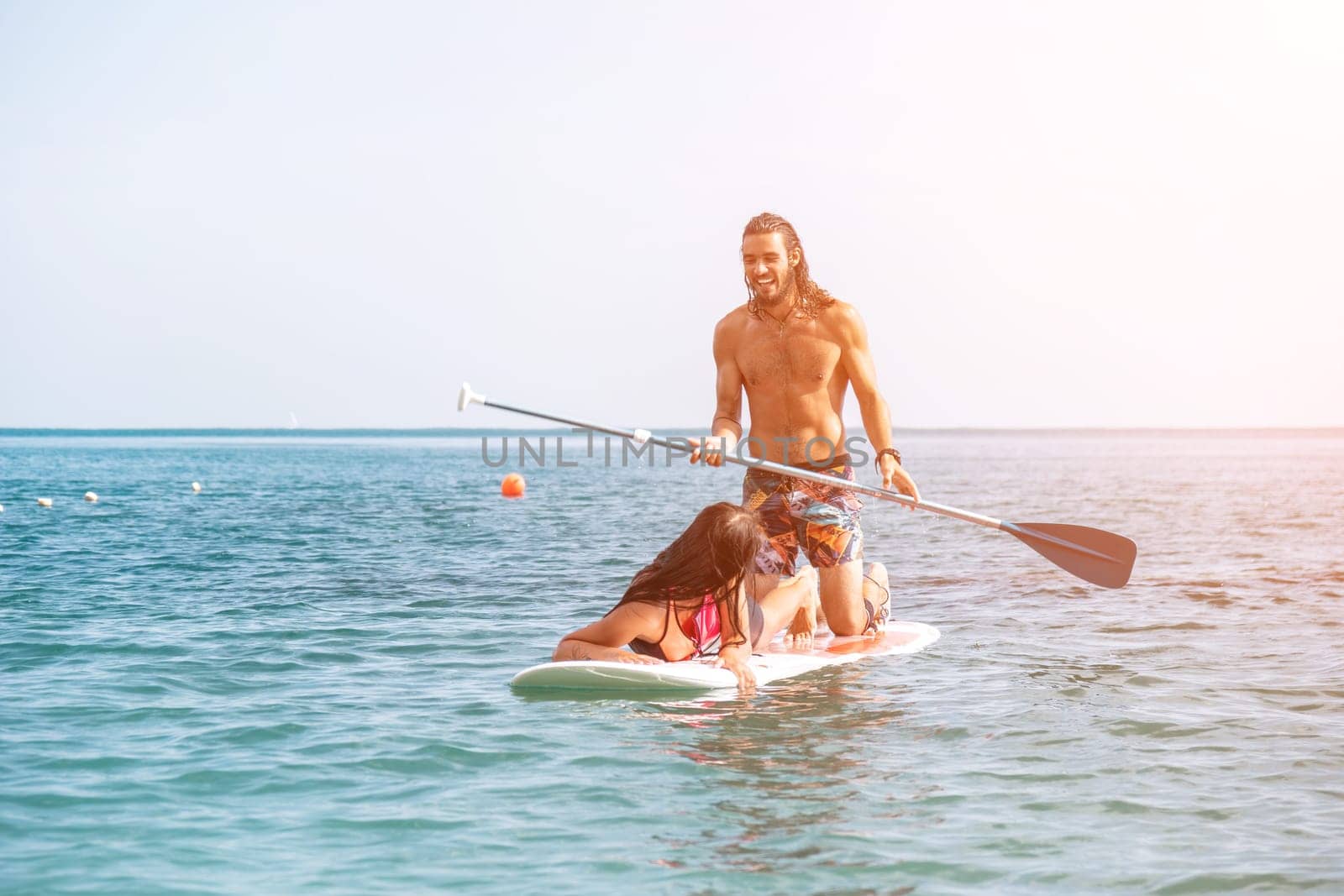 Sea woman and man on sup. Silhouette of happy young woman and man, surfing on SUP board, confident paddling through water surface. Idyllic sunset. Active lifestyle at sea or river. Slow motion by panophotograph