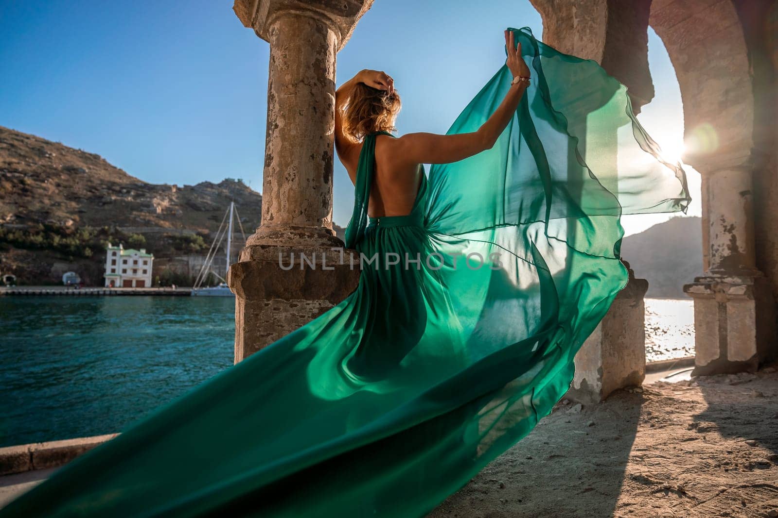 Woman dress sea columns. Rear view of a happy blonde woman in a long mint dress posing against the backdrop of the sea in an old building with columns