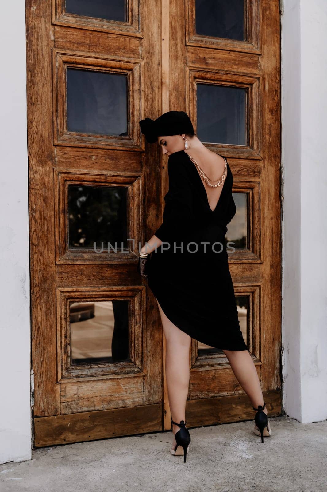Stylish woman in the city. Fashion photo of a beautiful model in an elegant black dress posing against the backdrop of a building on a city street.