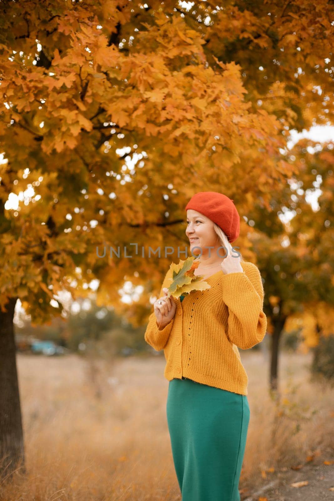 autumn woman in a red beret, yellow sweater and green skirt, against the background of an autumn tree.